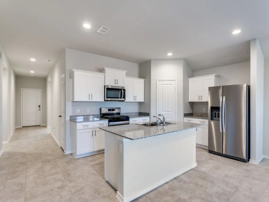 Kitchen with white cabinetry, stainless steel appliances, granite countertops, and a central island with an undermount sink