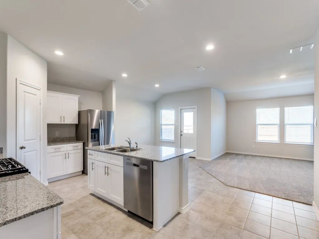 Open-concept kitchen with white cabinetry, granite countertops, stainless steel appliances, and an island with an integrated sink