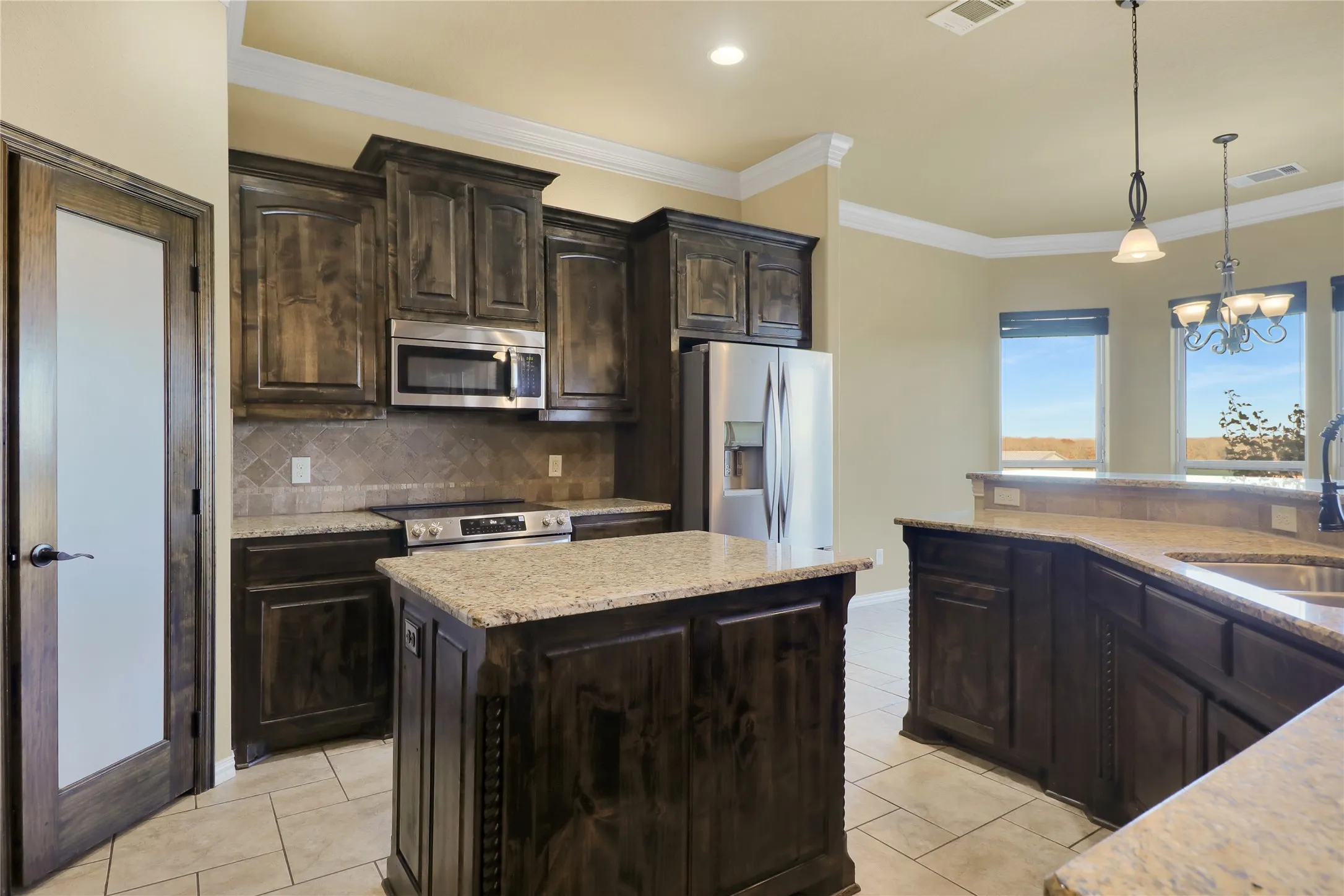 Spacious kitchen featuring dark wood cabinetry, stainless steel appliances, granite countertops, and tile flooring