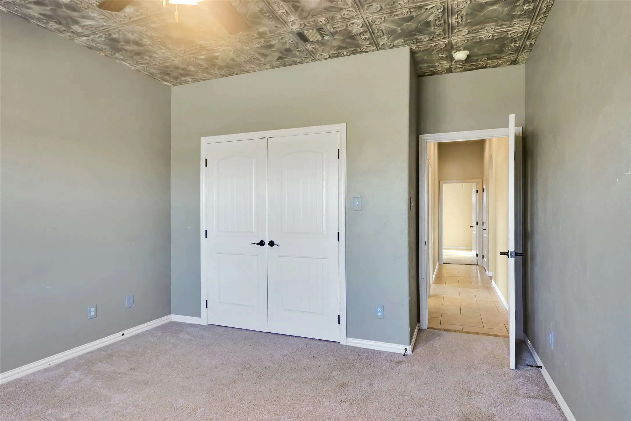 Textured ceiling paneling, light gray painted walls, carpeting, and white paneled double doors with black hardware