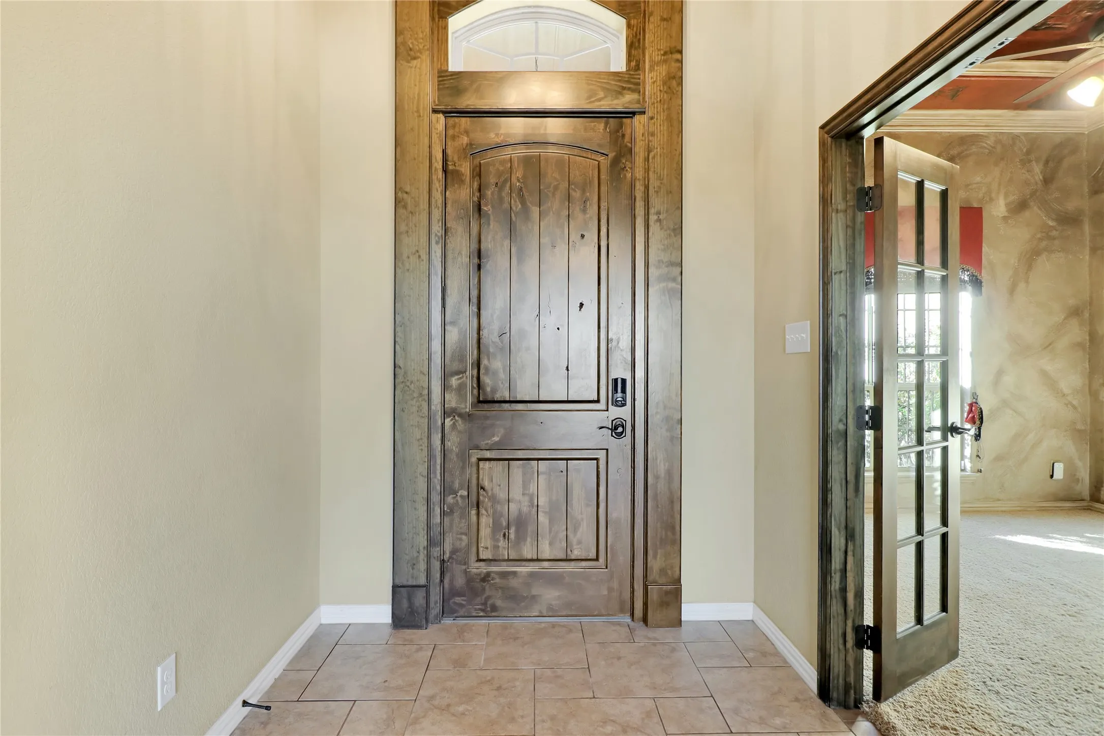 Arched transom window above a paneled wood entry door, complemented by a tile flooring entry