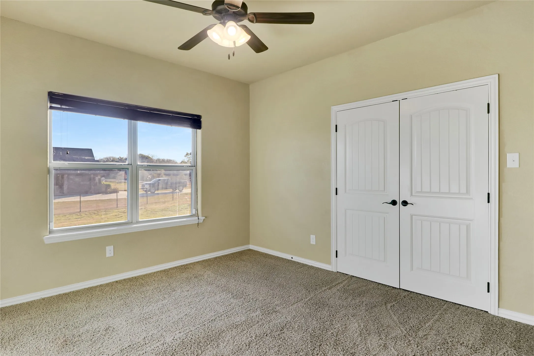 Neutral tone walls, carpeted flooring, a ceiling fan with light fixture, a window with a roller shade, and white double doors with arch-top paneling