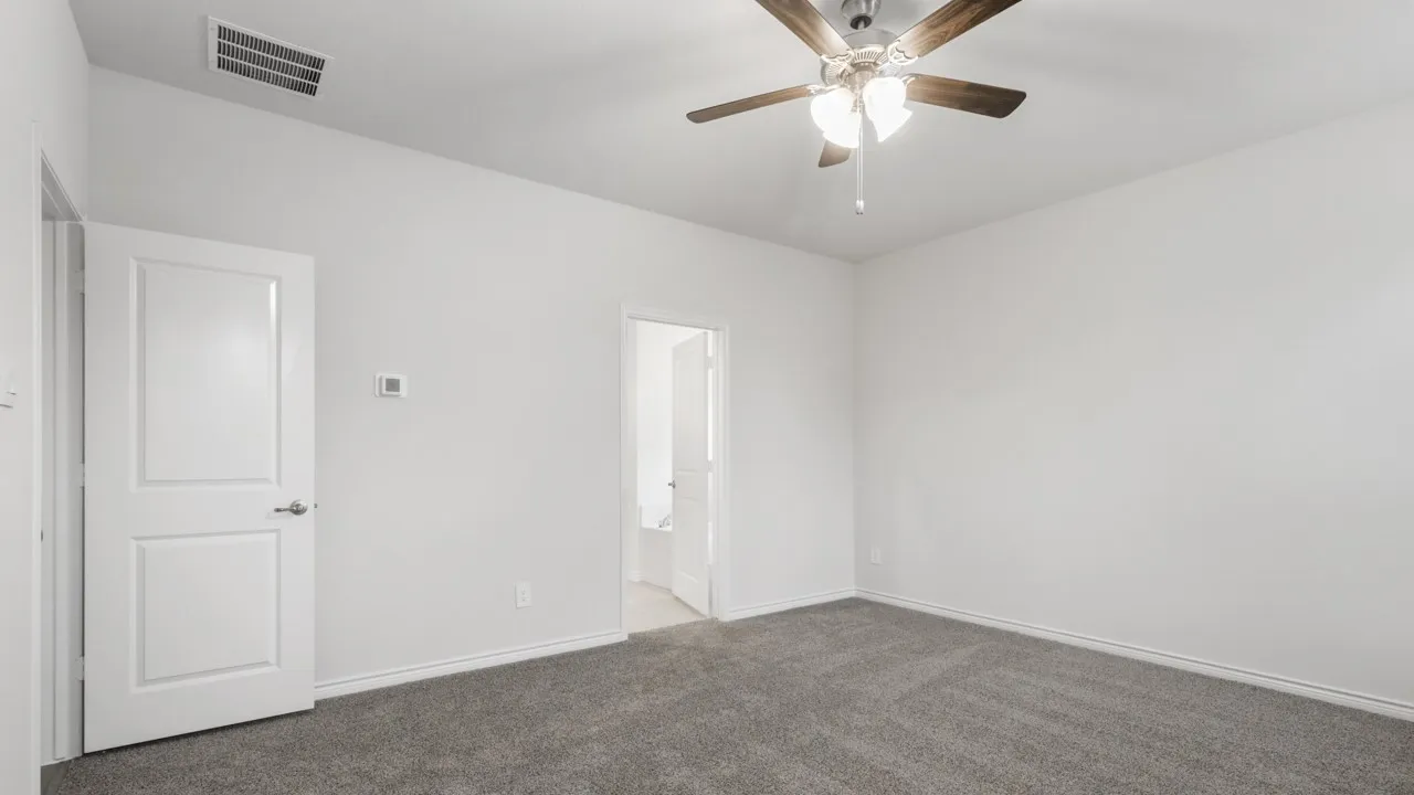 Spacious room featuring gray carpeting, white walls, a ceiling fan with light fixture, and a modern thermostat