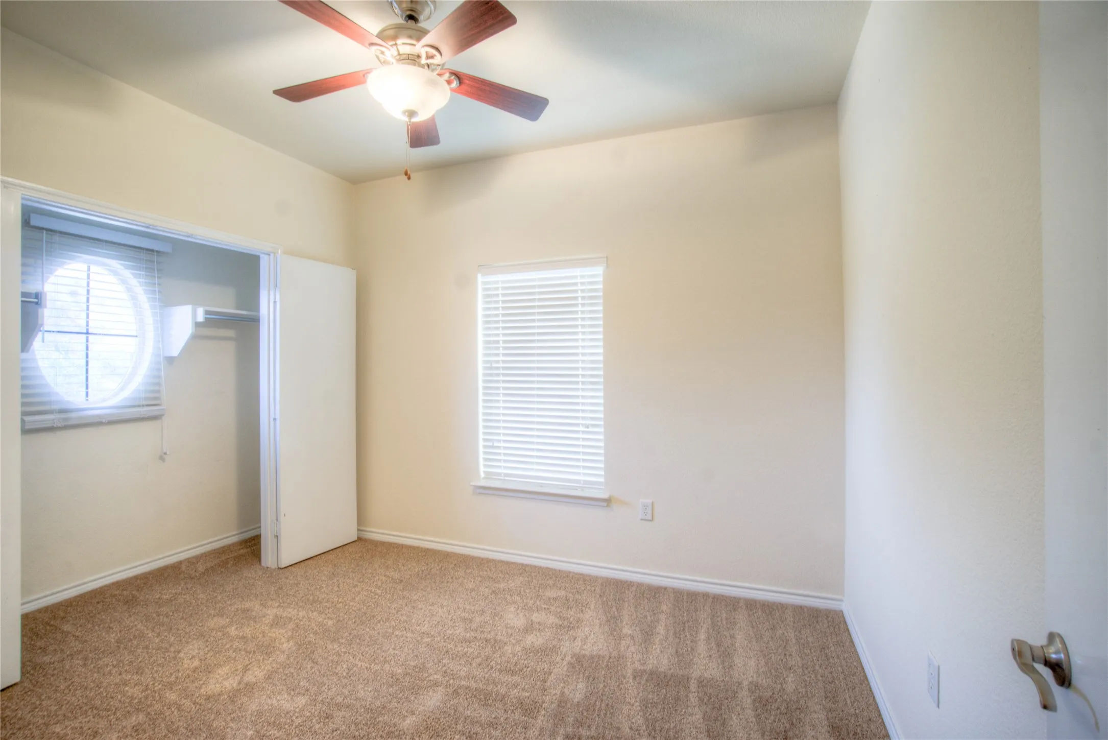 Neutral toned walls and carpeting with a ceiling fan