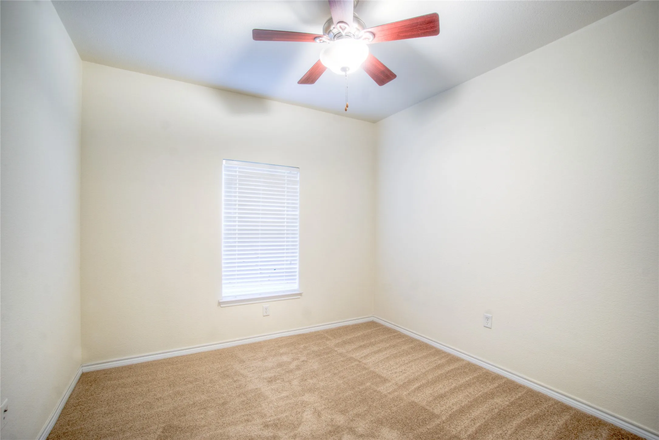 Neutral-toned carpeting, ceiling fan with light fixture, and a window with blinds