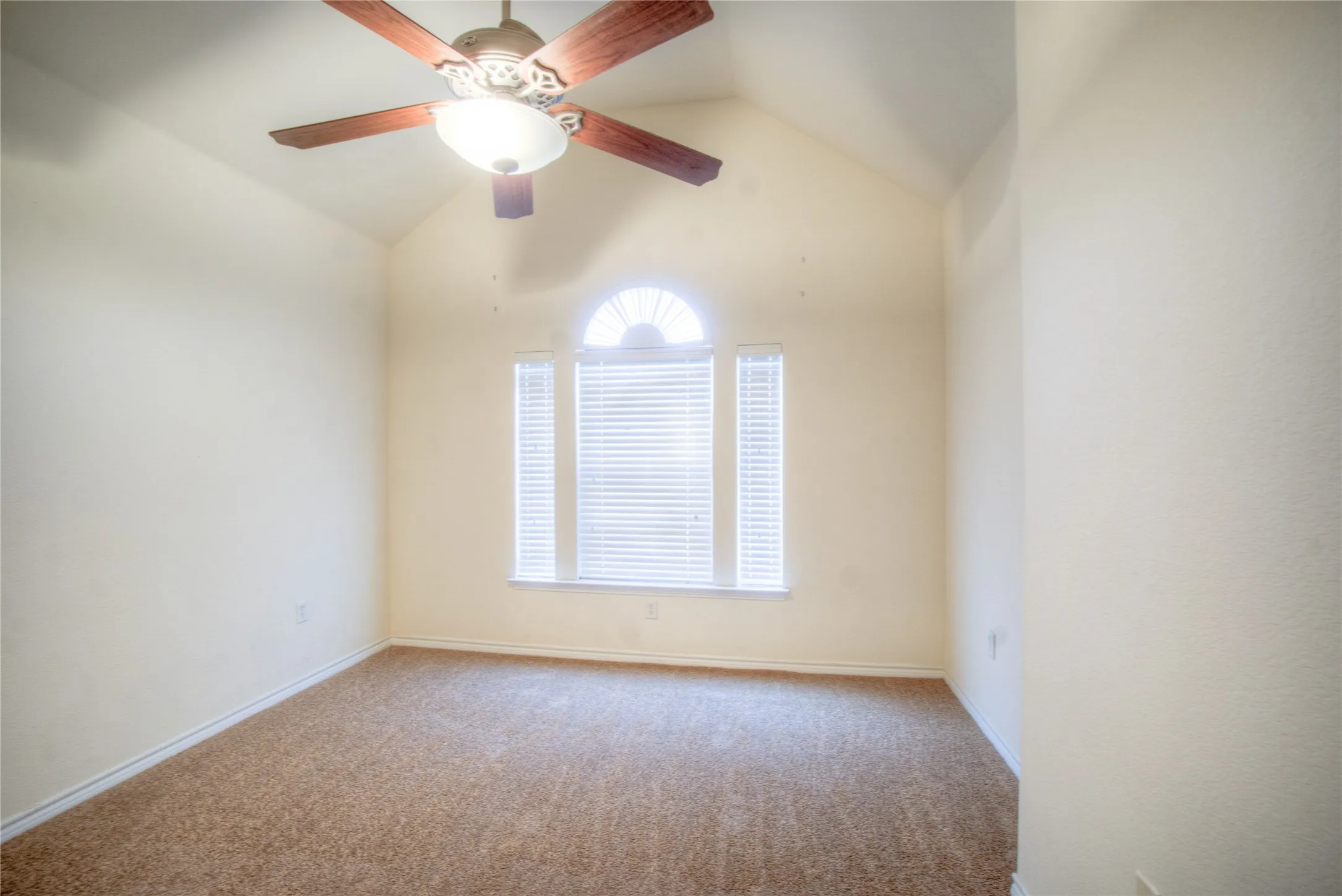 Vaulted ceiling, arched window accent, window blinds, ceiling fan with integrated lighting, and carpeted flooring