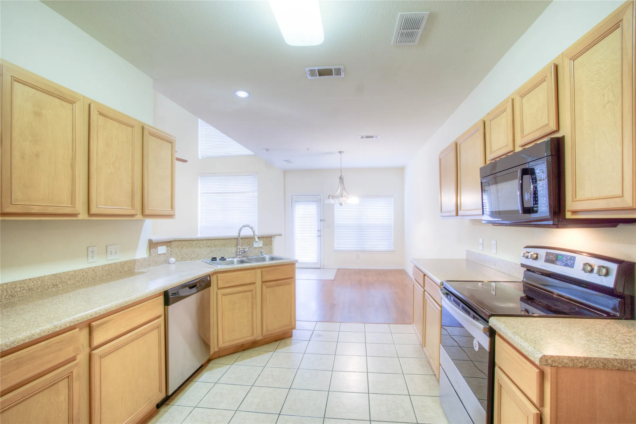 Kitchen featuring wood-finish cabinetry, light-toned countertops, tile flooring, and integrated stainless steel appliances including a dishwasher, range, and microwave