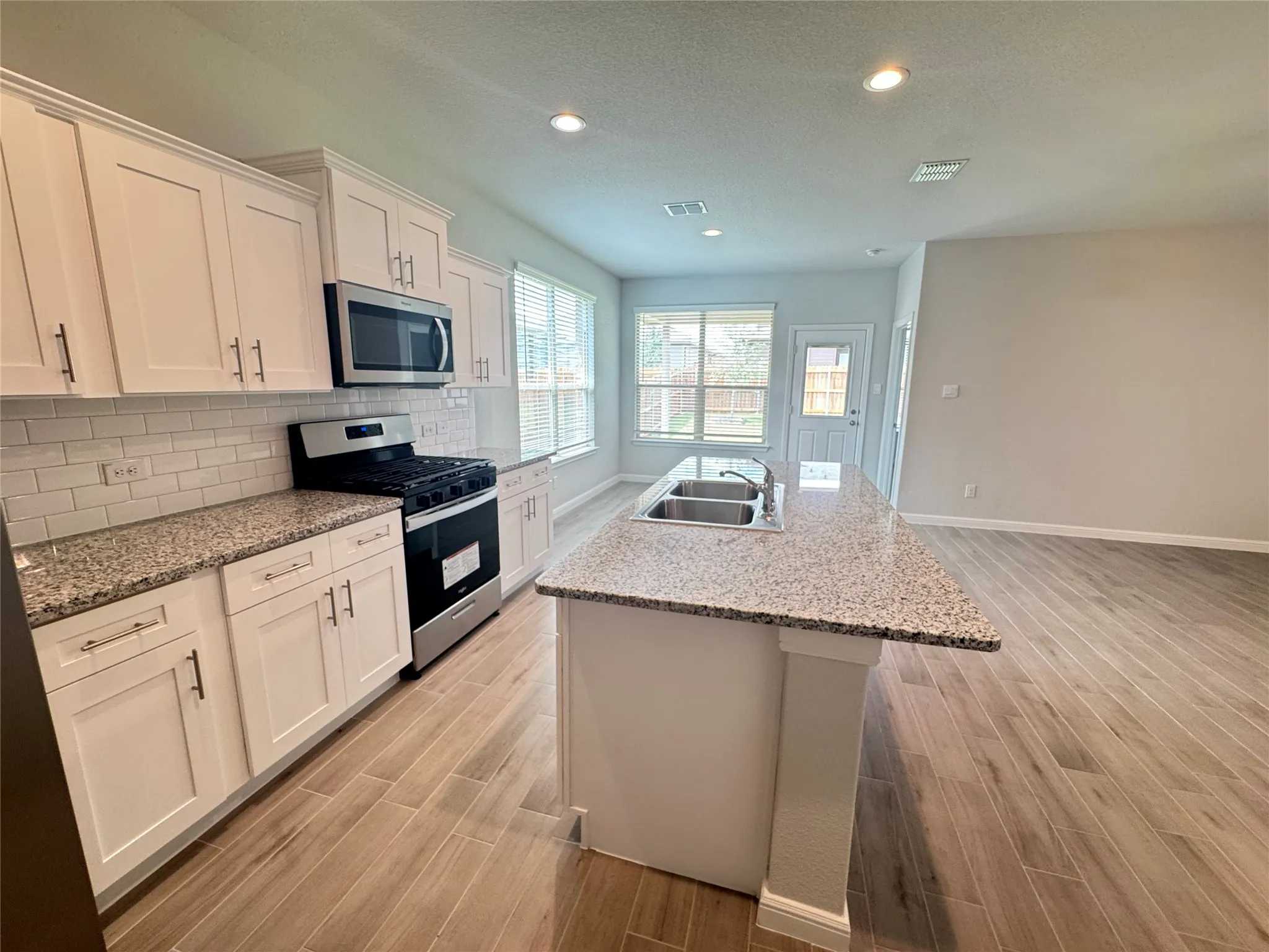 Kitchen featuring appliances with stainless steel finishes, a sink, light wood-style flooring, an island with sink, and white cabinets