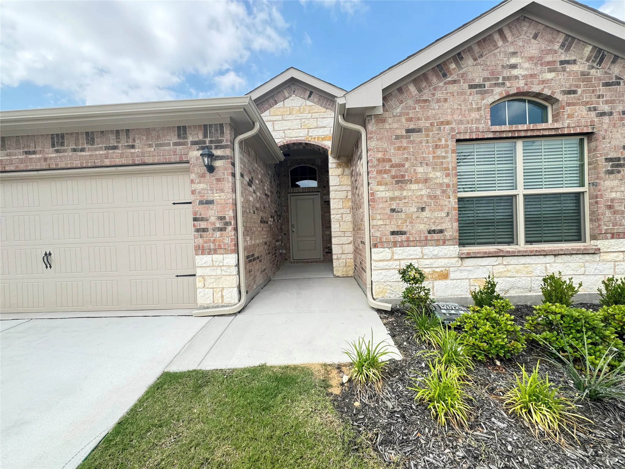 Entrance to property with an attached garage, stone siding, driveway, and brick siding