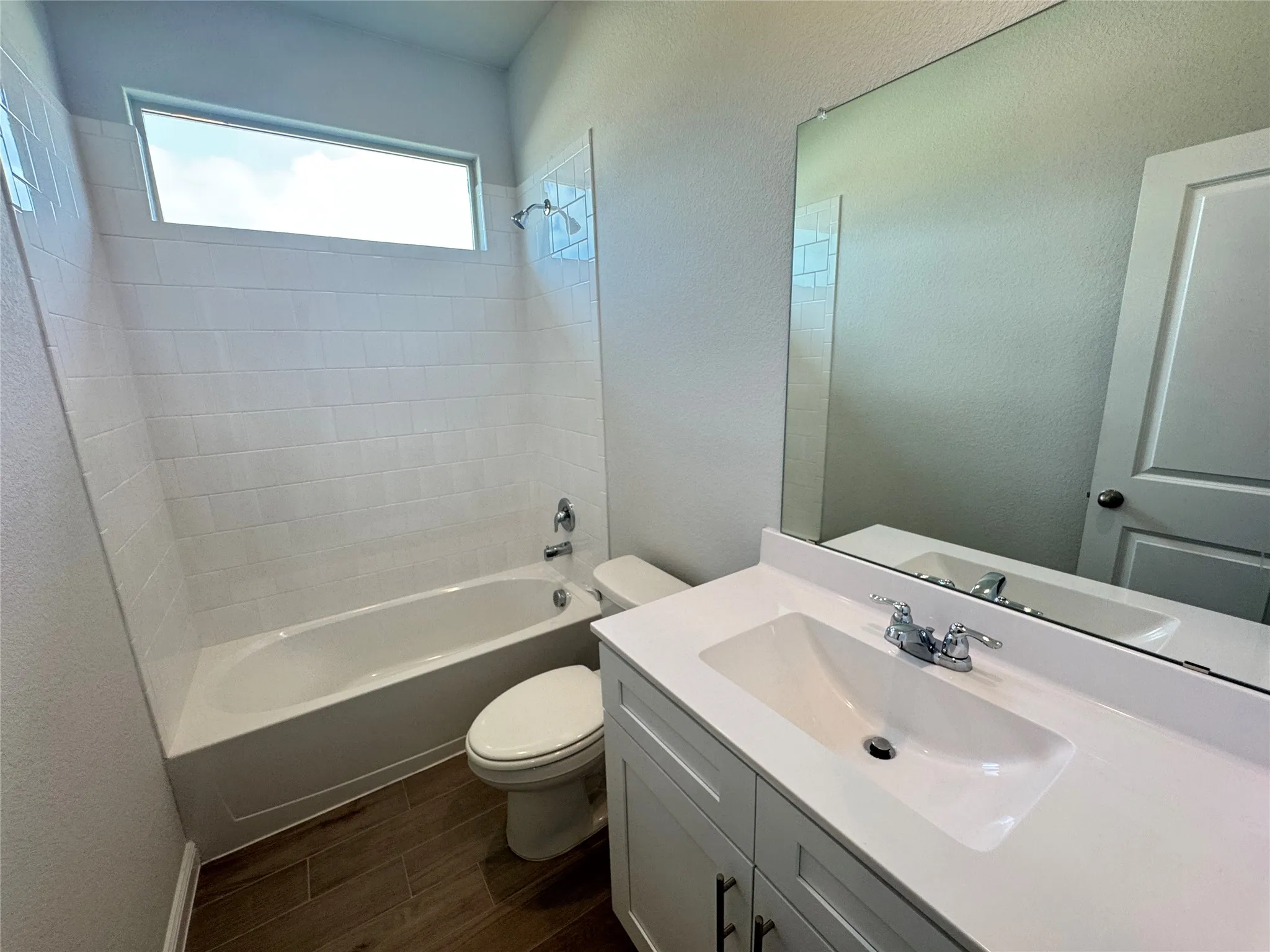 Bathroom with toilet, shower / tub combination, vanity, wood finished floors, and a textured wall