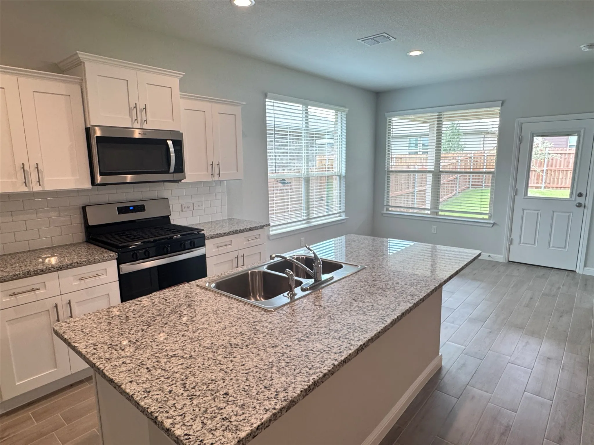 Kitchen featuring stainless steel appliances, a sink, wood tiled floors, white cabinets, and decorative backsplash