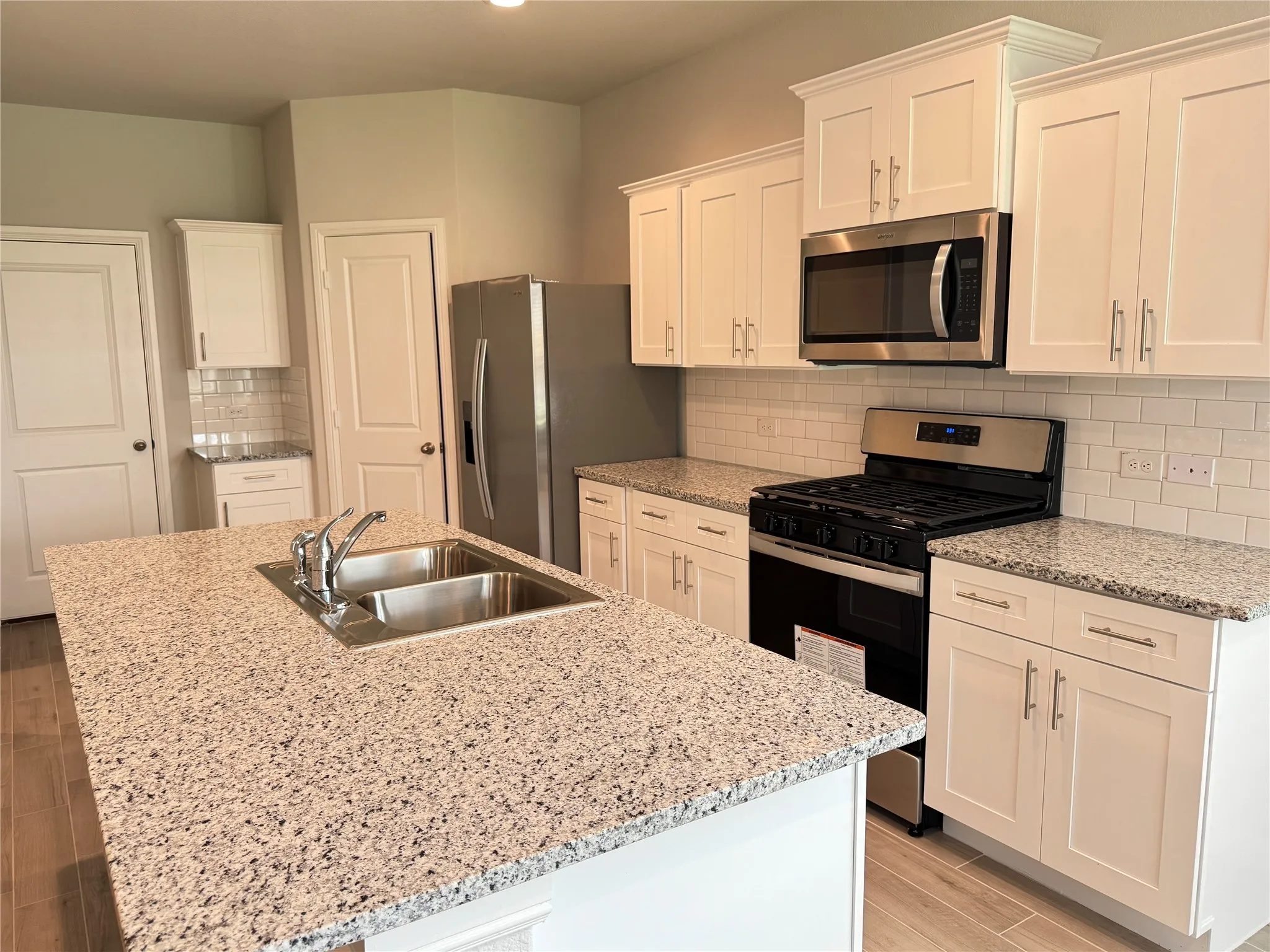 Kitchen featuring appliances with stainless steel finishes, a sink, white cabinetry, light wood-style floors, and an island with sink