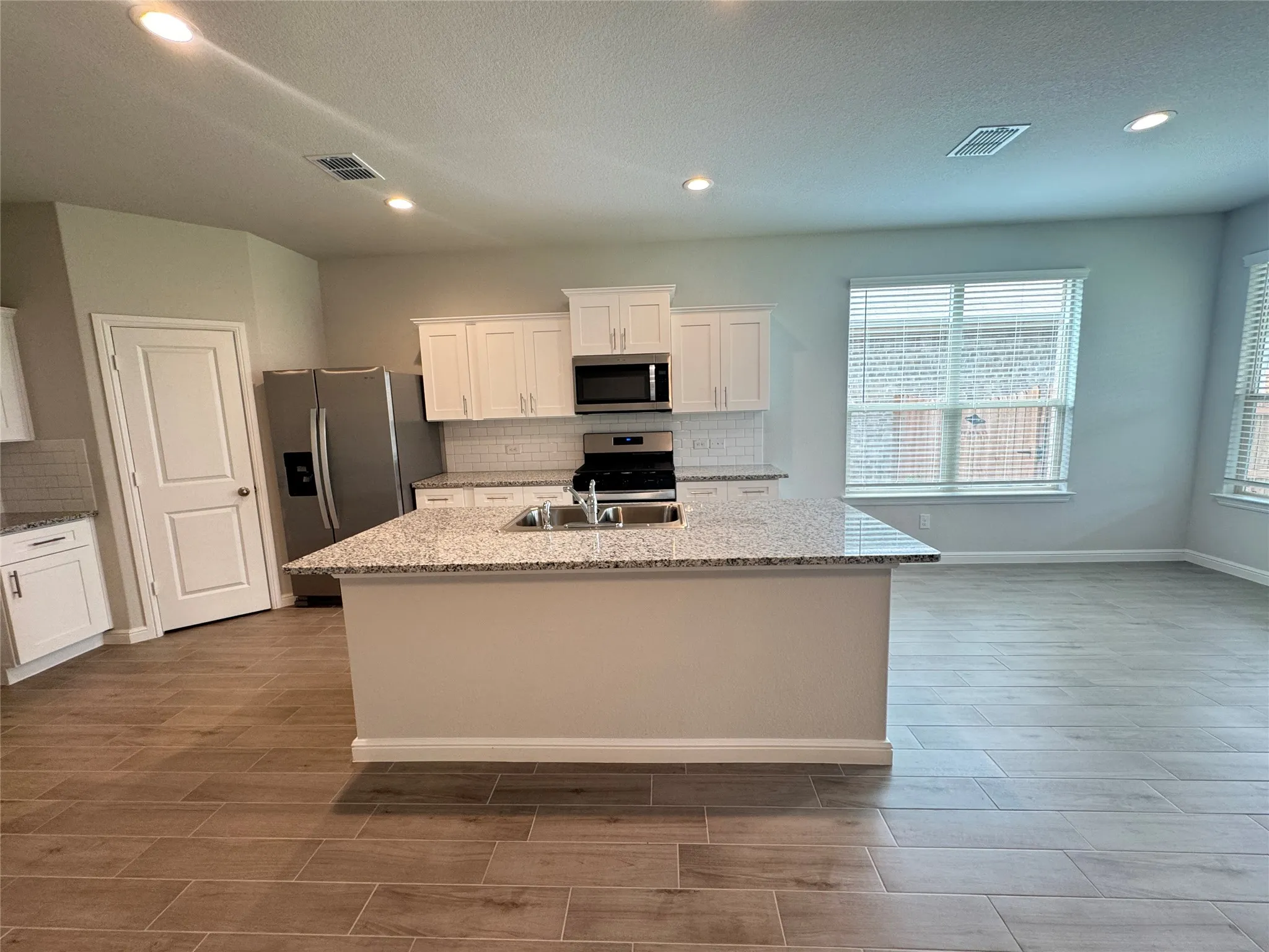 Kitchen featuring stainless steel appliances, decorative backsplash, white cabinetry, a sink, and a kitchen island with sink