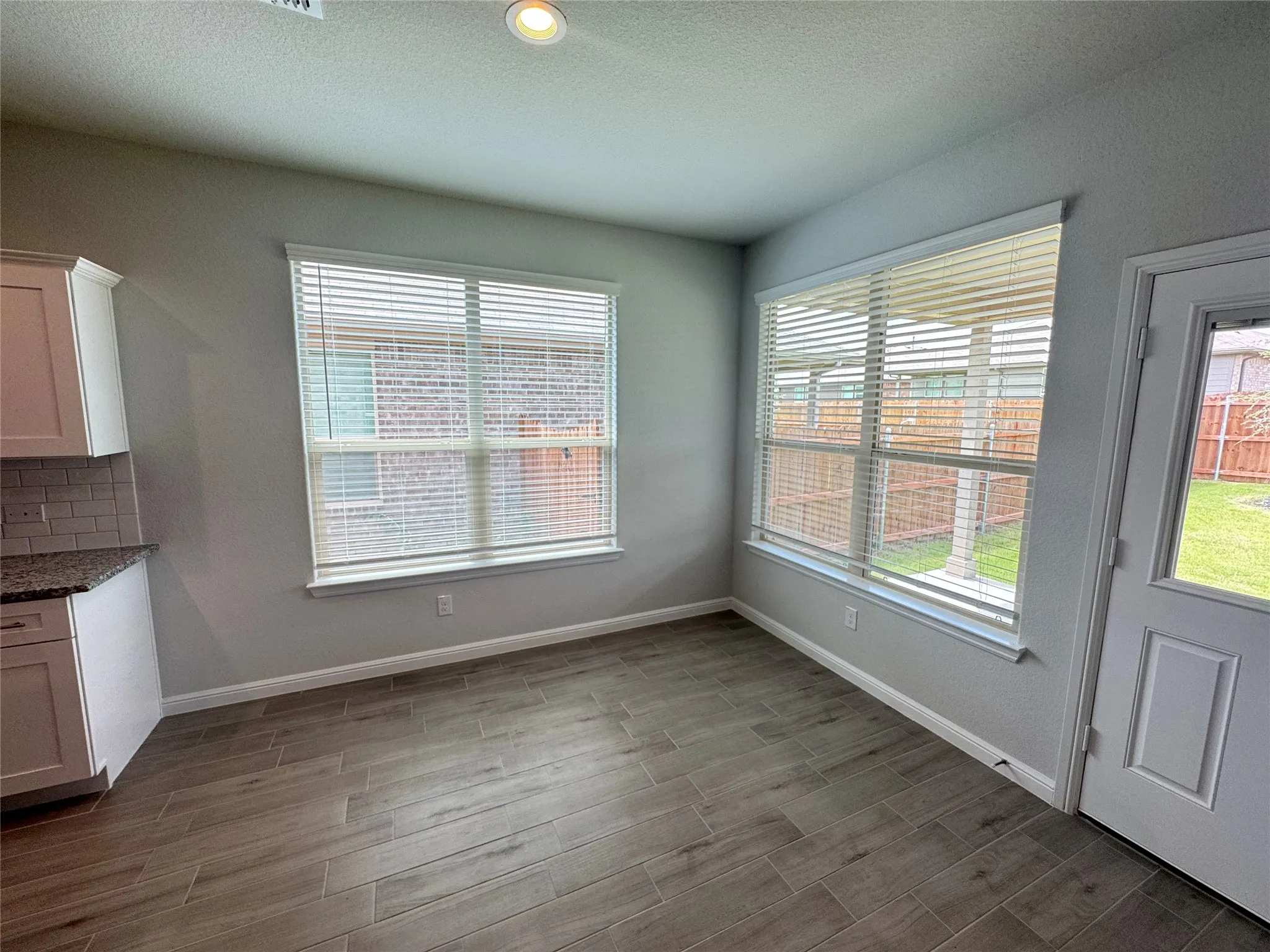 Unfurnished dining area featuring healthy amount of natural light, wood finished floors, baseboards, and a textured ceiling