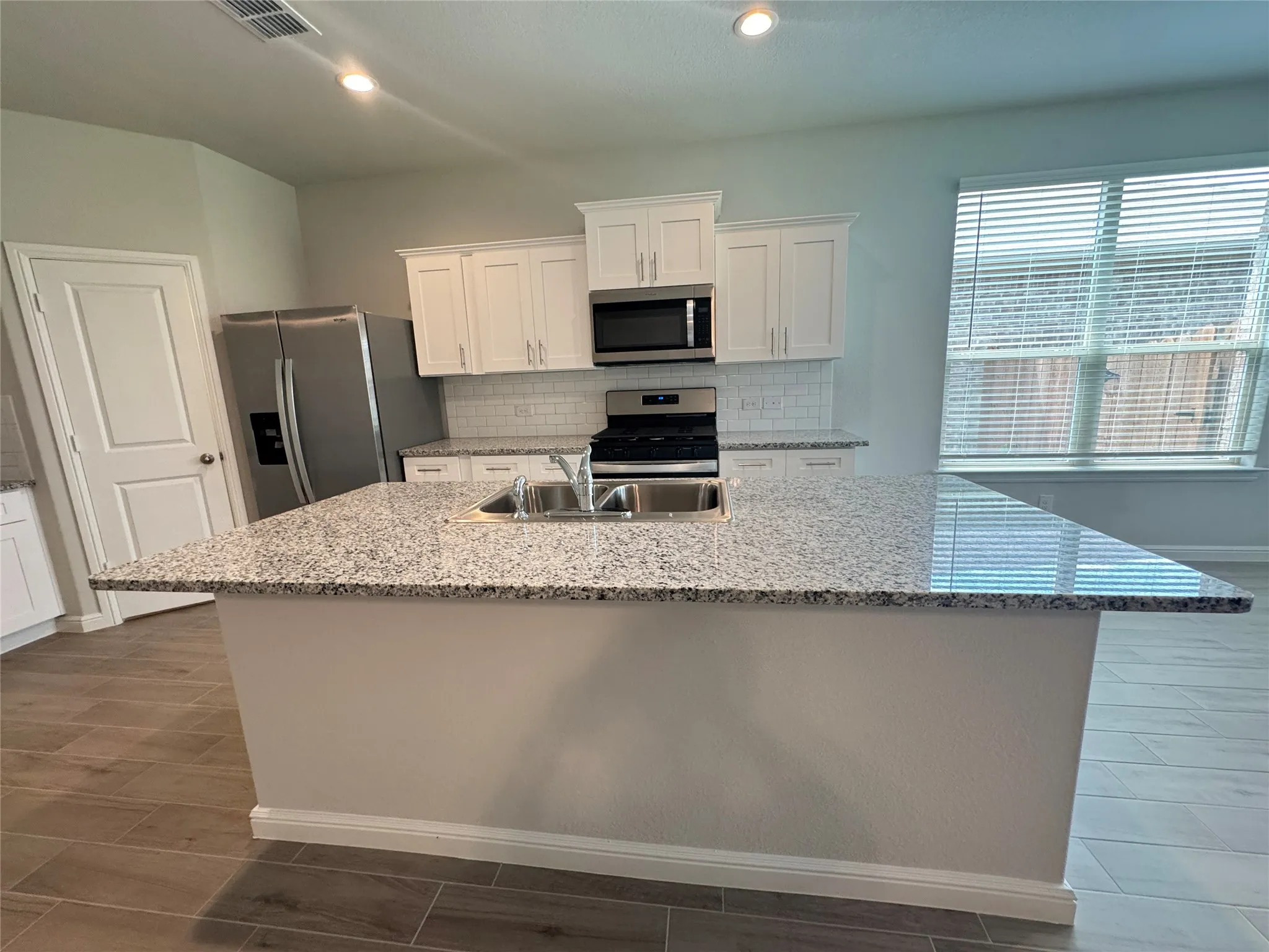 Kitchen with appliances with stainless steel finishes, a sink, white cabinetry, an island with sink, and baseboards