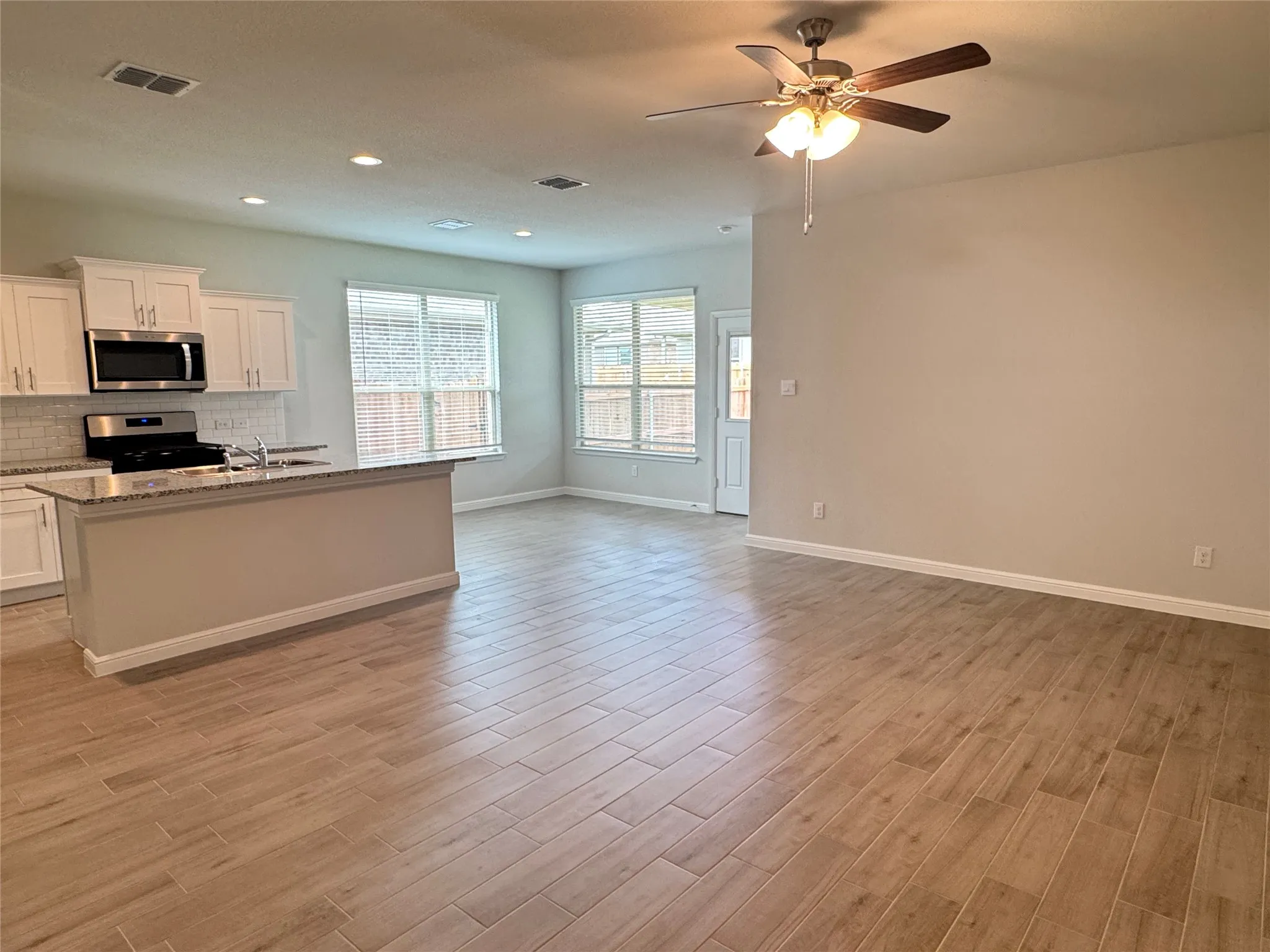Kitchen featuring stainless steel appliances, open floor plan, a ceiling fan, baseboards, and light wood-style flooring