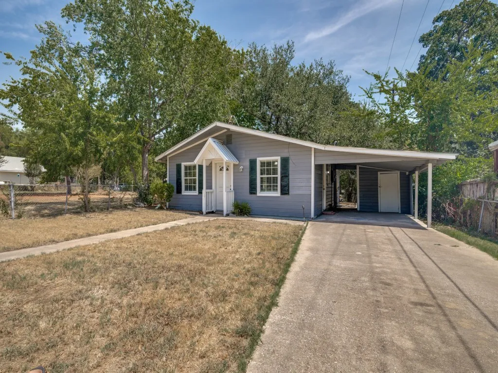 Gray siding exterior with white trim, covered front porch, dark green window shutters, and a covered carport