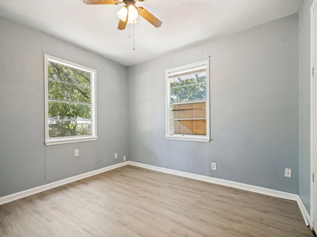 Wood-finish flooring, white trim, and a ceiling fan with integrated lighting