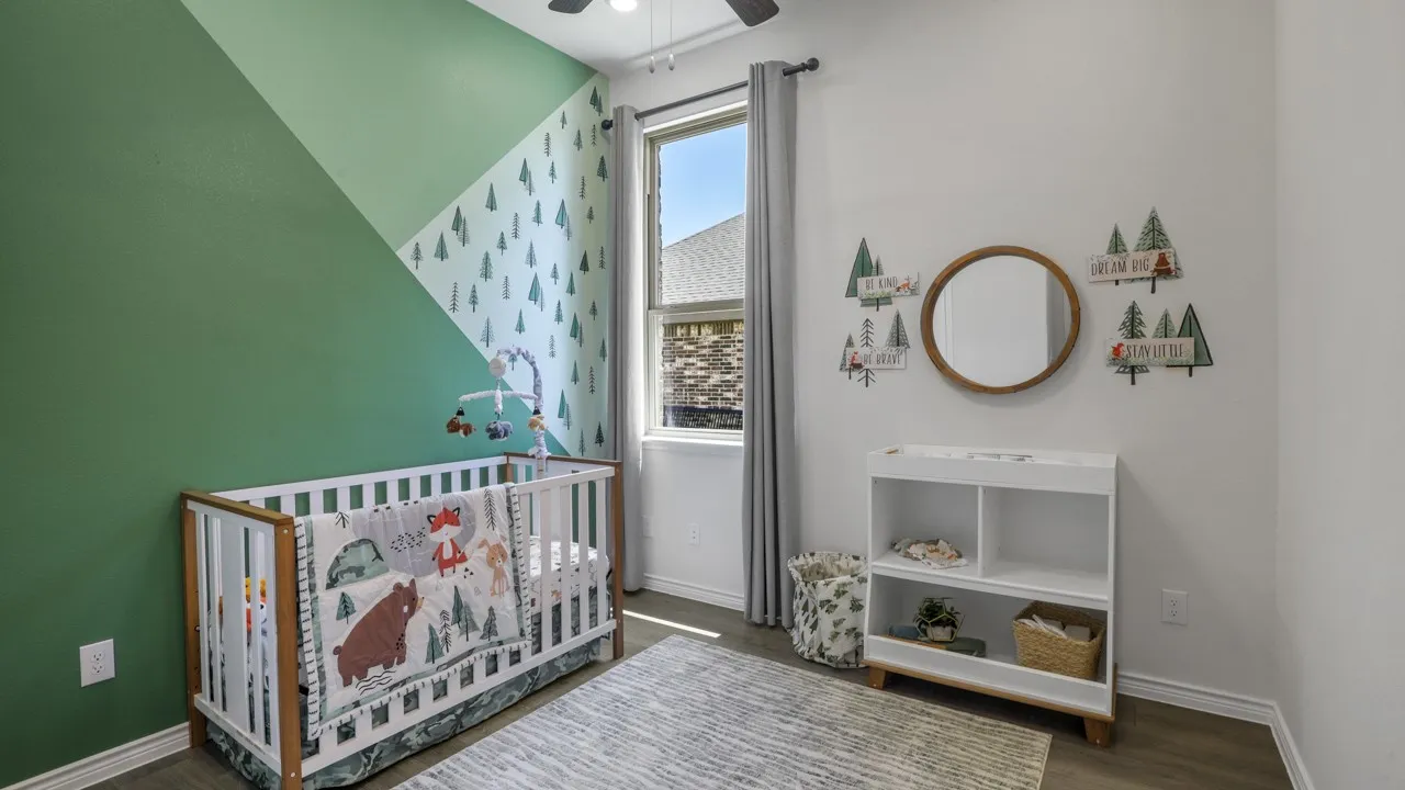 Bright nursery featuring a color-blocked accent wall in soft green, large glass door with natural light, wood-finish flooring, and built-in storage shelving with open cubbies for organization and display