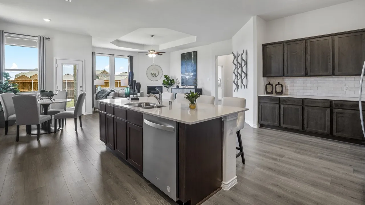 Kitchen island with an undermount sink, stainless steel dishwasher, wood-finish flooring, and dark wood cabinetry