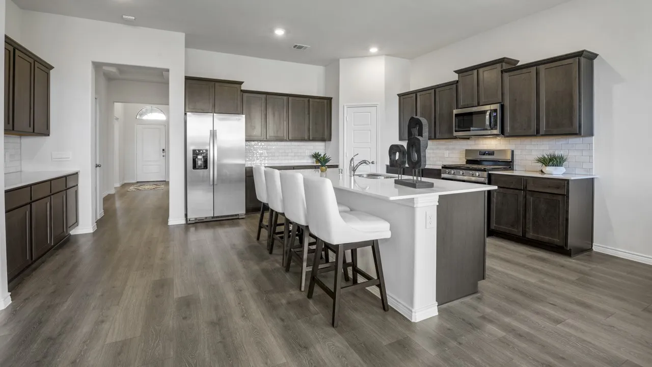Kitchen featuring wood-finish flooring, dark wood-finish cabinetry, stainless steel appliances, a center island with a sink, and a white subway tile backsplash