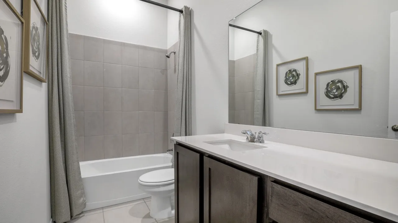White vanity countertop with an integrated sink, dark wood-finish cabinetry, a full-width mirror, and a tiled shower-tub combination