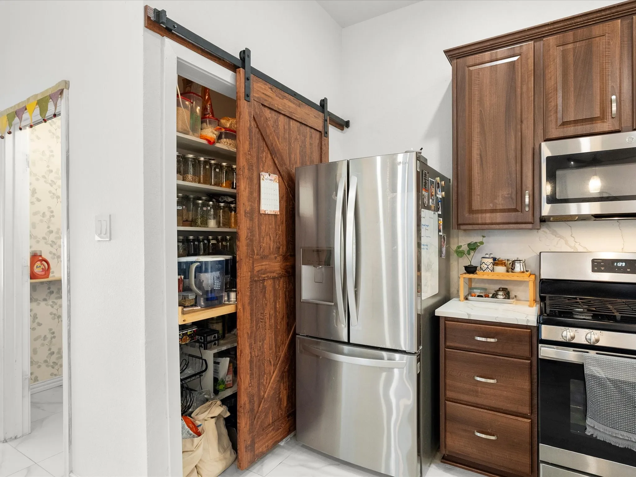 Kitchen featuring wood-finish cabinetry, built-in stainless steel appliances, and a barn door pantry