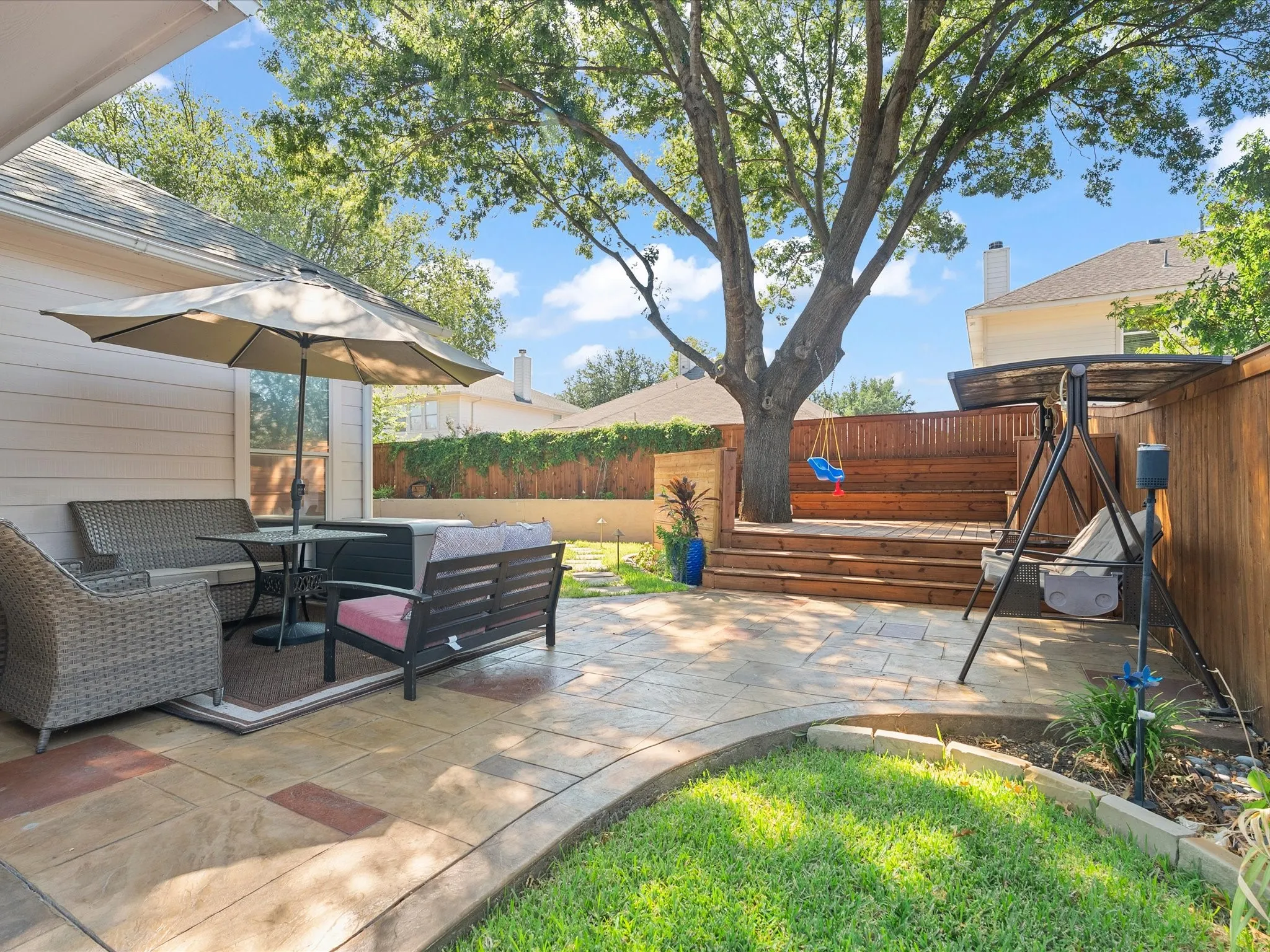 Expansive backyard featuring a stamped concrete patio, tiered wood deck, mature shade tree, and wood privacy fencing