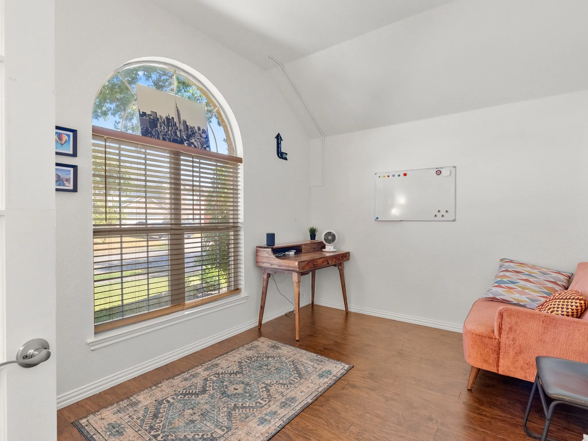 Vaulted ceiling, arched window with blinds, wood-finish flooring, and white walls