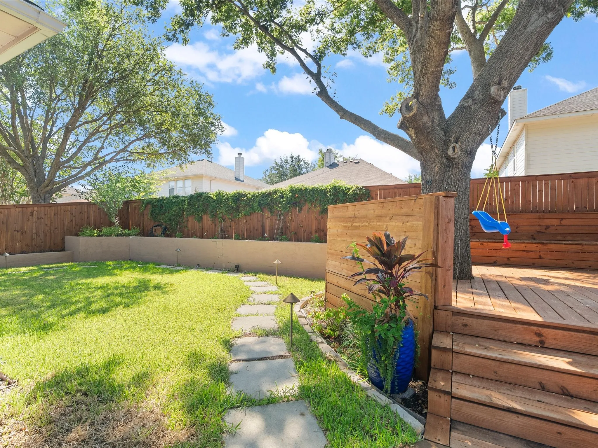 Expansive backyard featuring a manicured lawn, established shade trees, wood decking, and a stone pathway