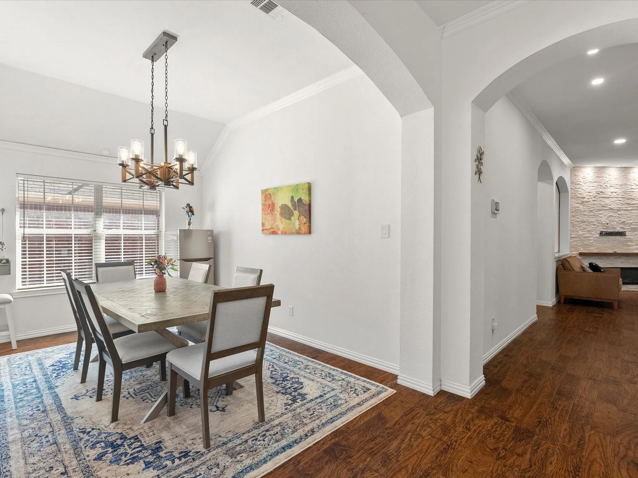 Vaulted ceiling with an architectural chandelier, wood-finish flooring, window with blinds, and arched doorways