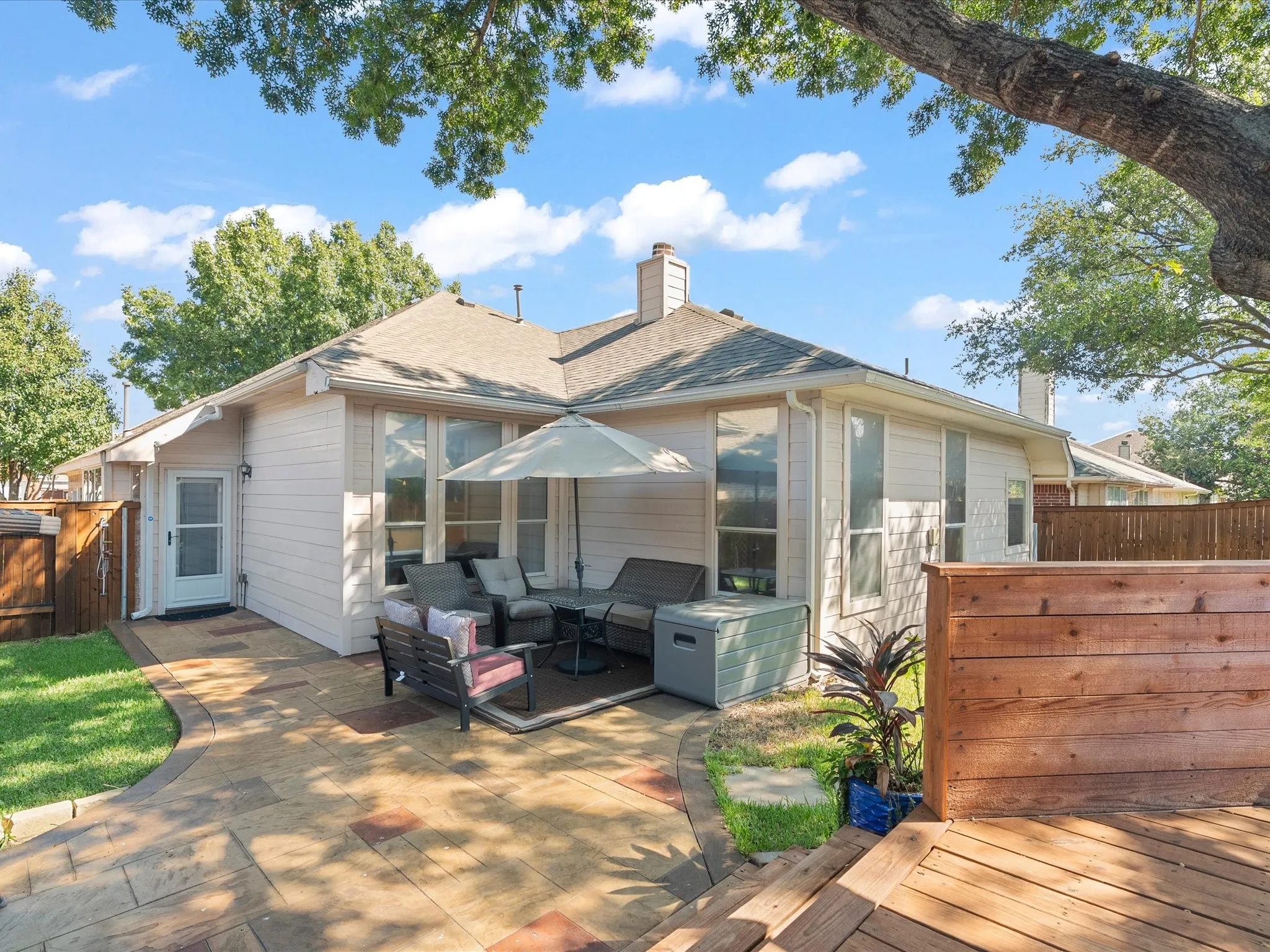 Exterior featuring light-colored siding, a shingled roof, multiple windows, a patterned paver patio, and a wooden deck