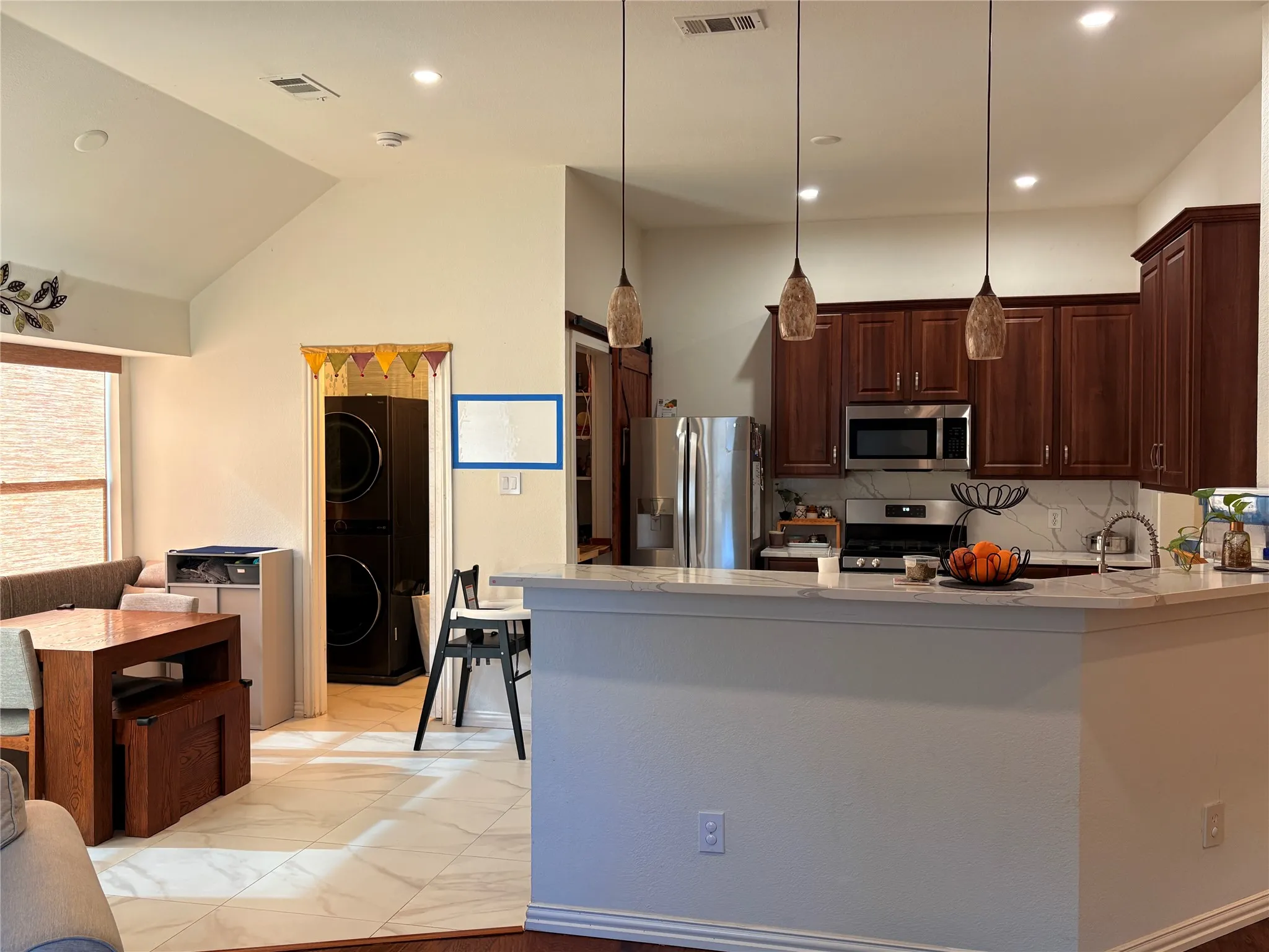 Vaulted ceiling with recessed lighting, kitchen with dark wood cabinetry, stainless steel appliances, stone countertops, and tile flooring
