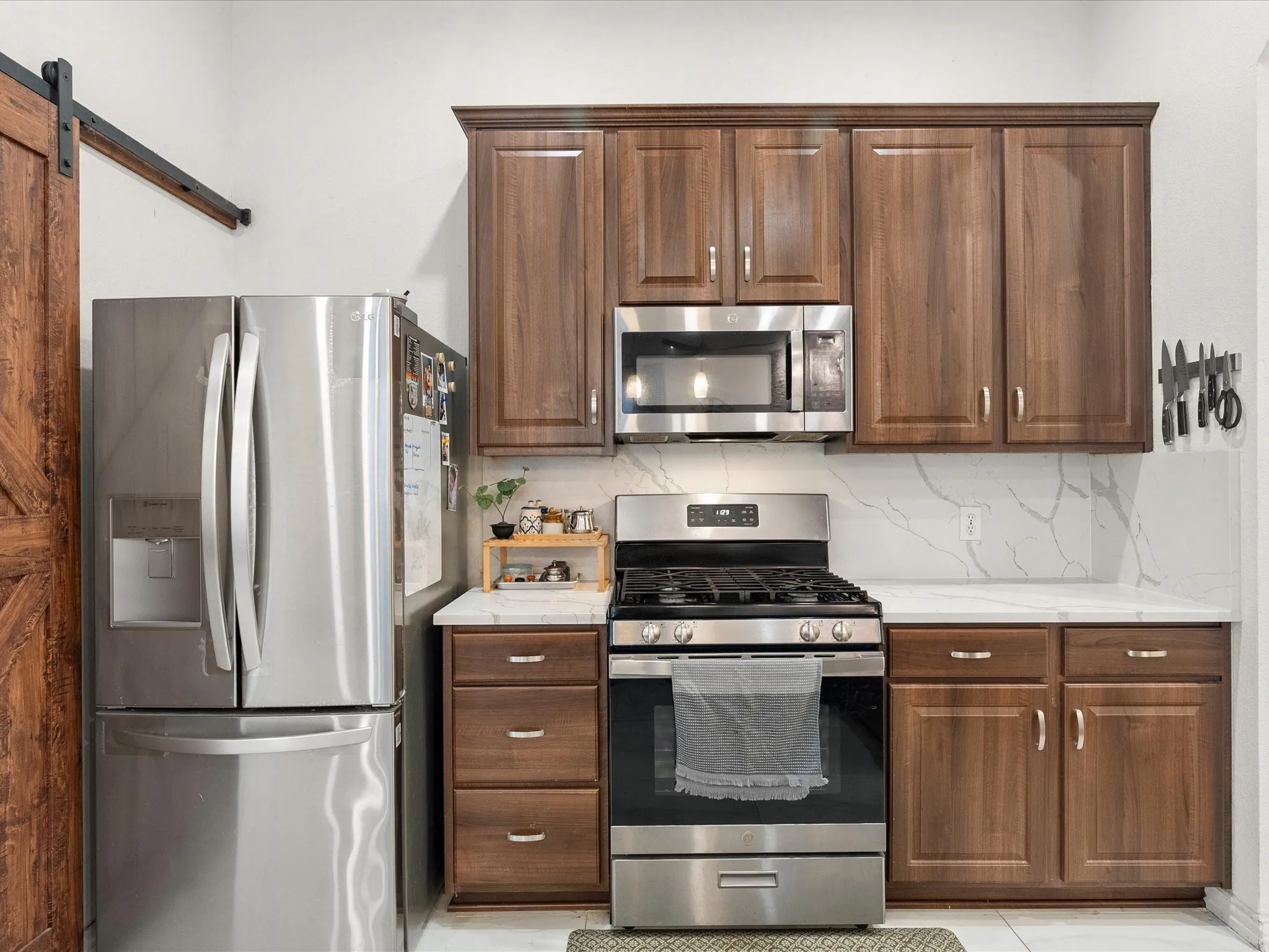 Stainless steel appliances with wood-finish cabinetry, white countertops, and a full-height backsplash