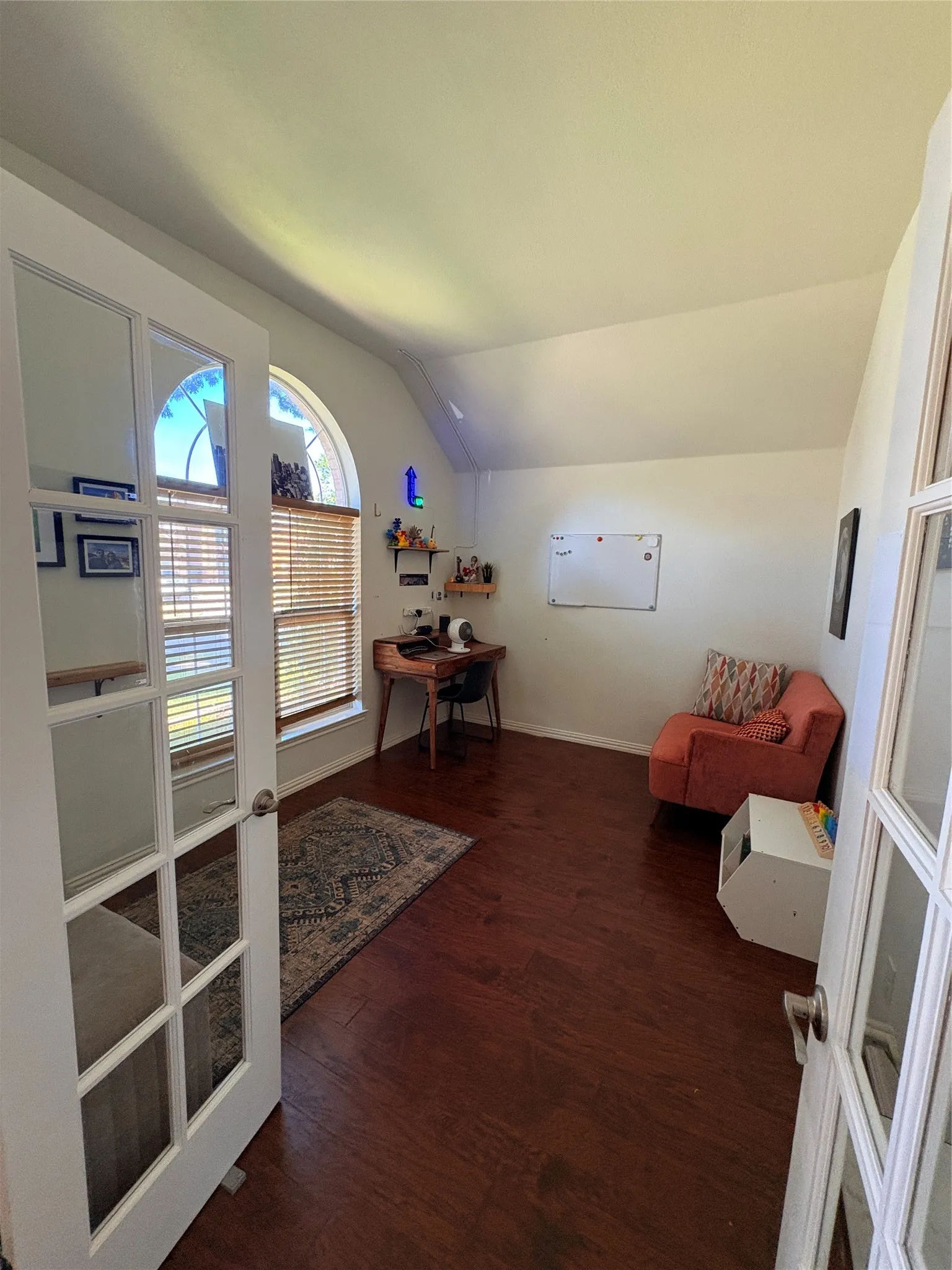 Wood-finish flooring throughout, arched window with horizontal blinds, and a vaulted ceiling