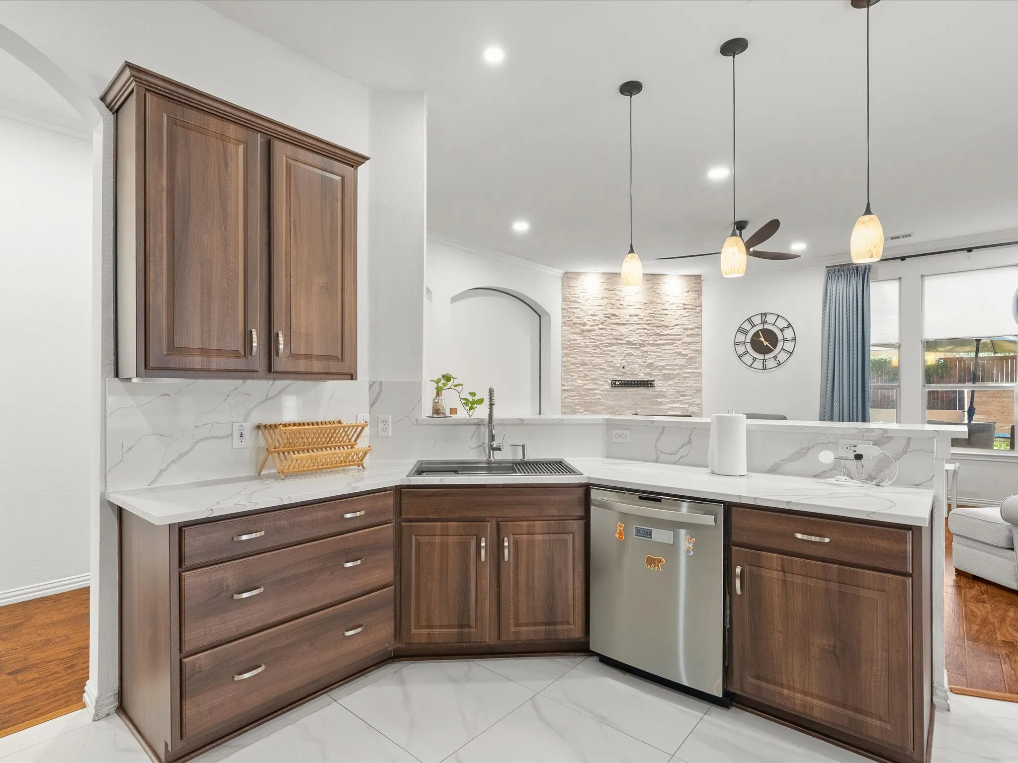 Kitchen with dark wood-finish cabinetry, white countertops, a stainless steel dishwasher, and a white tile backsplash