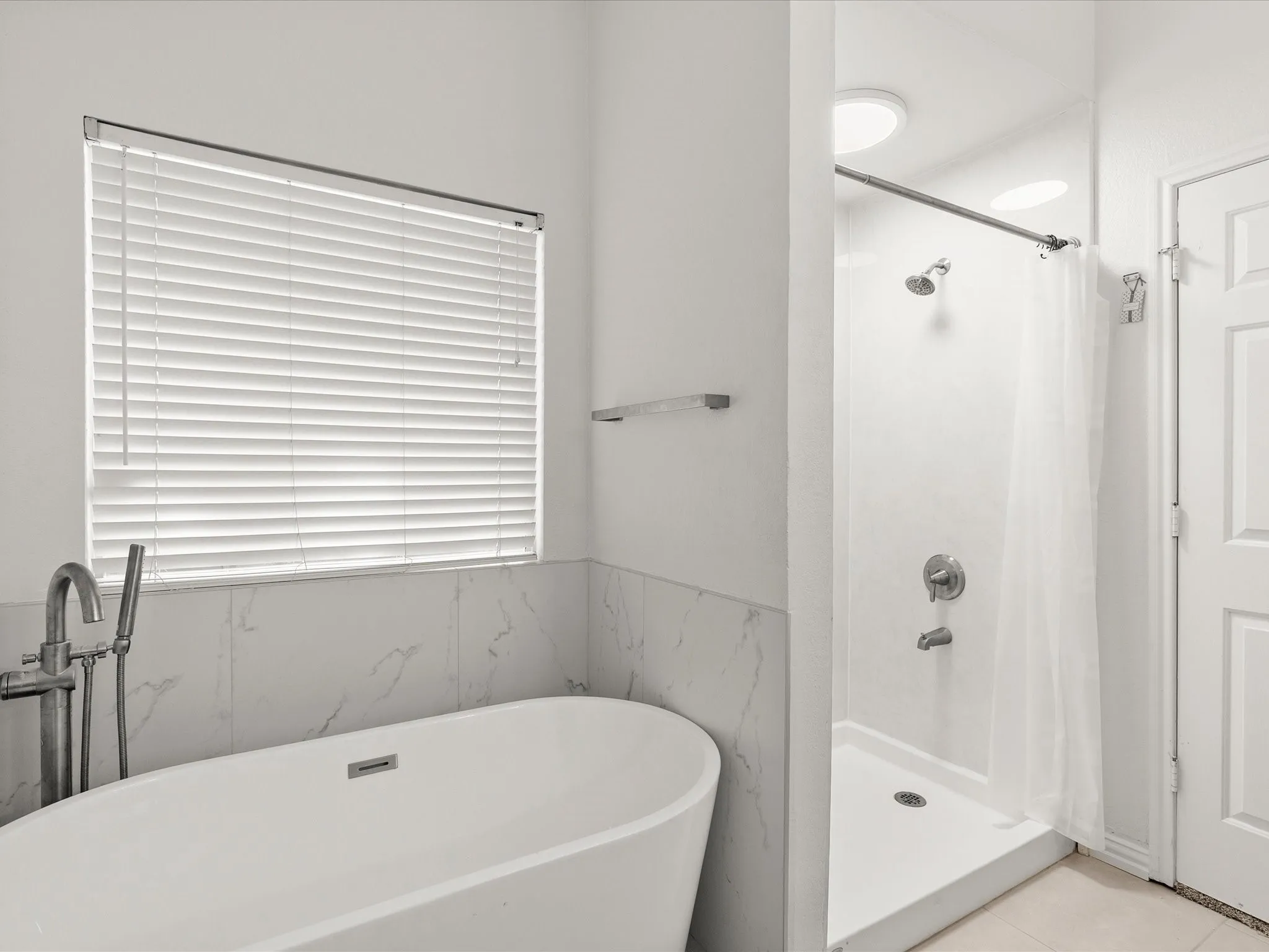 Freestanding soaking tub with a floor-mounted faucet, complemented by a separate shower stall with a single showerhead and an integrated light fixture