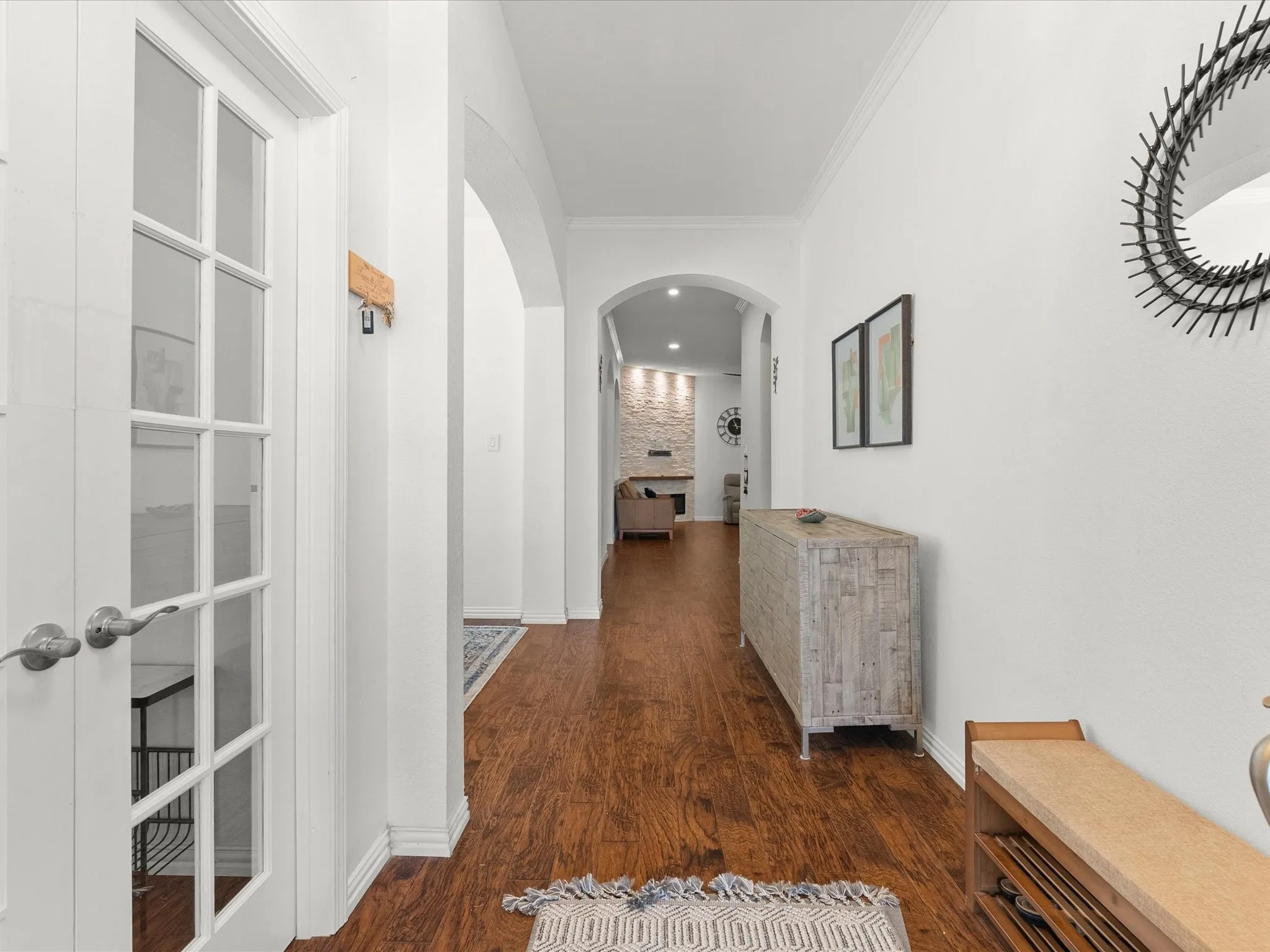Wood-finish flooring throughout, complemented by a white paneled door with glass inserts, and arched doorways