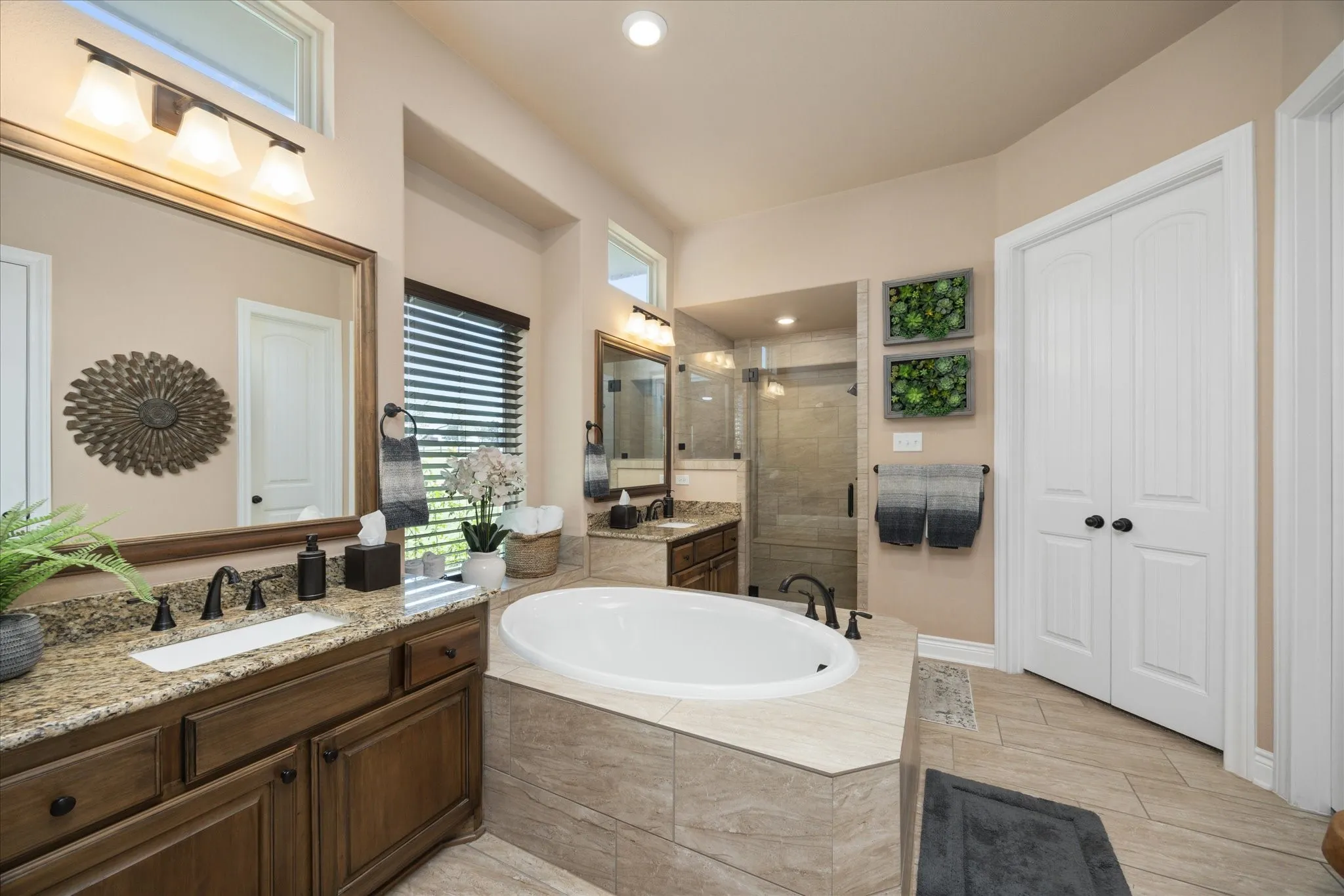 Dual vanities with granite countertops, wood-finish cabinetry, built-in soaking tub, walk-in shower with glass enclosure, and tile flooring