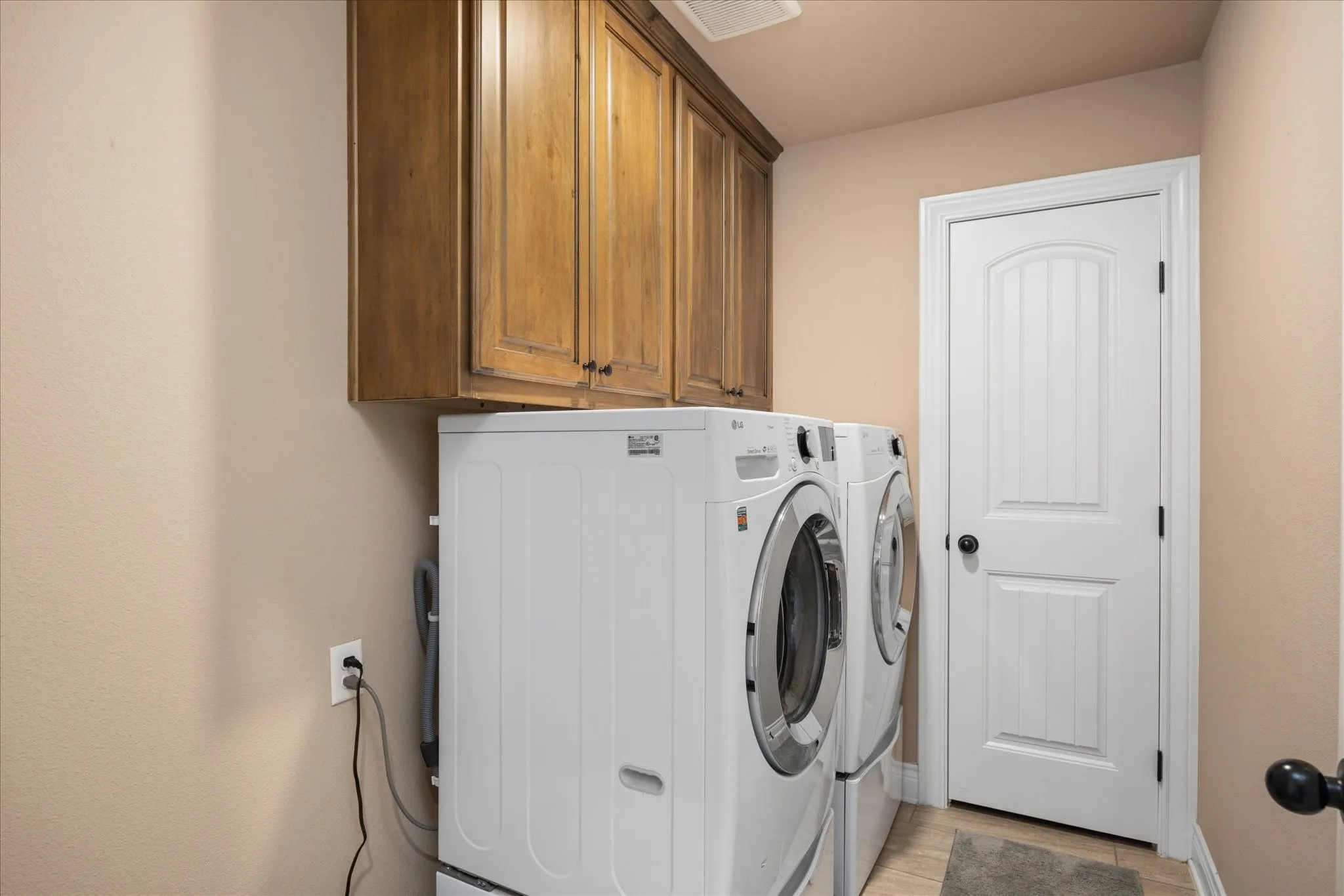 Overhead wood-finish cabinetry, light-toned wall paint, and a paneled white door with matte black hardware