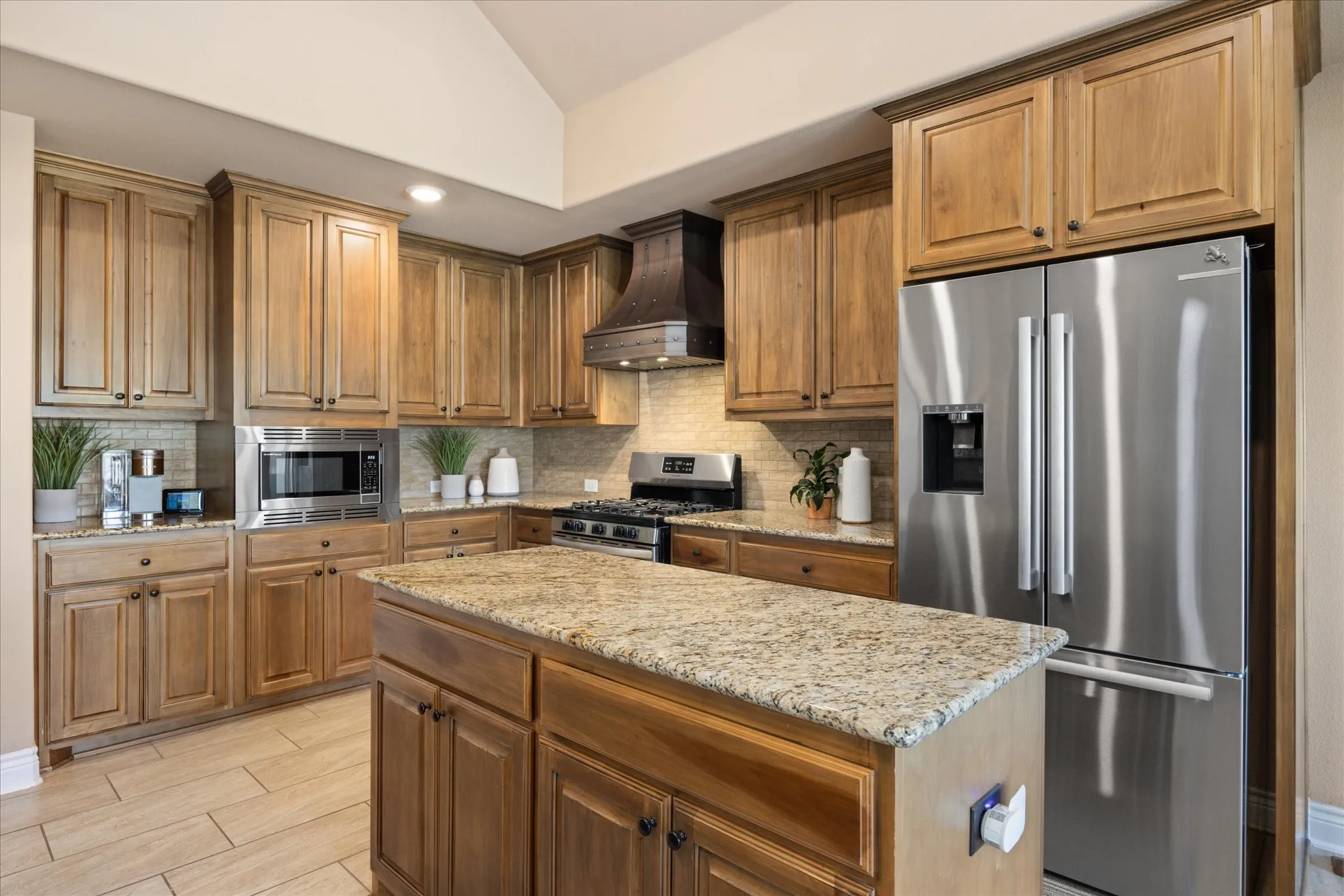 Wood cabinetry, stainless steel appliances, stone countertops, tile backsplash, and a central island