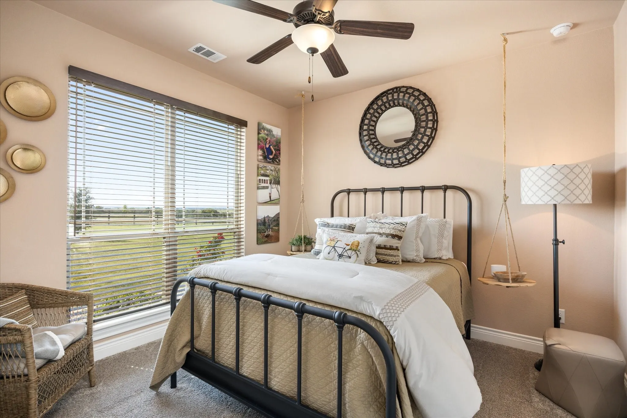 Large window with horizontal blinds, overhead ceiling fan with integrated lighting, wall-mounted circular mirror, and neutral wall paint