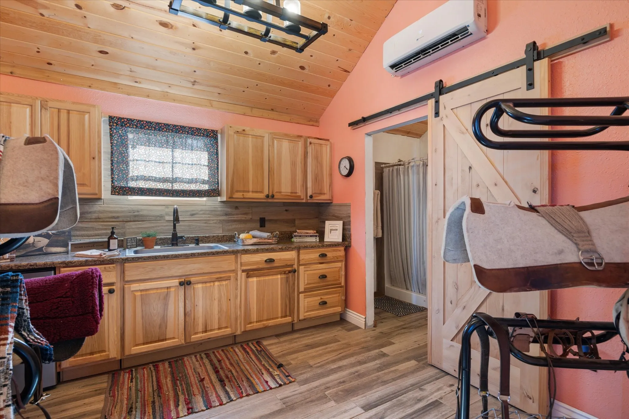 Light wood-finish flooring, natural wood cabinetry, wood plank ceiling, natural stone backsplash, and a barn door leading to an additional space