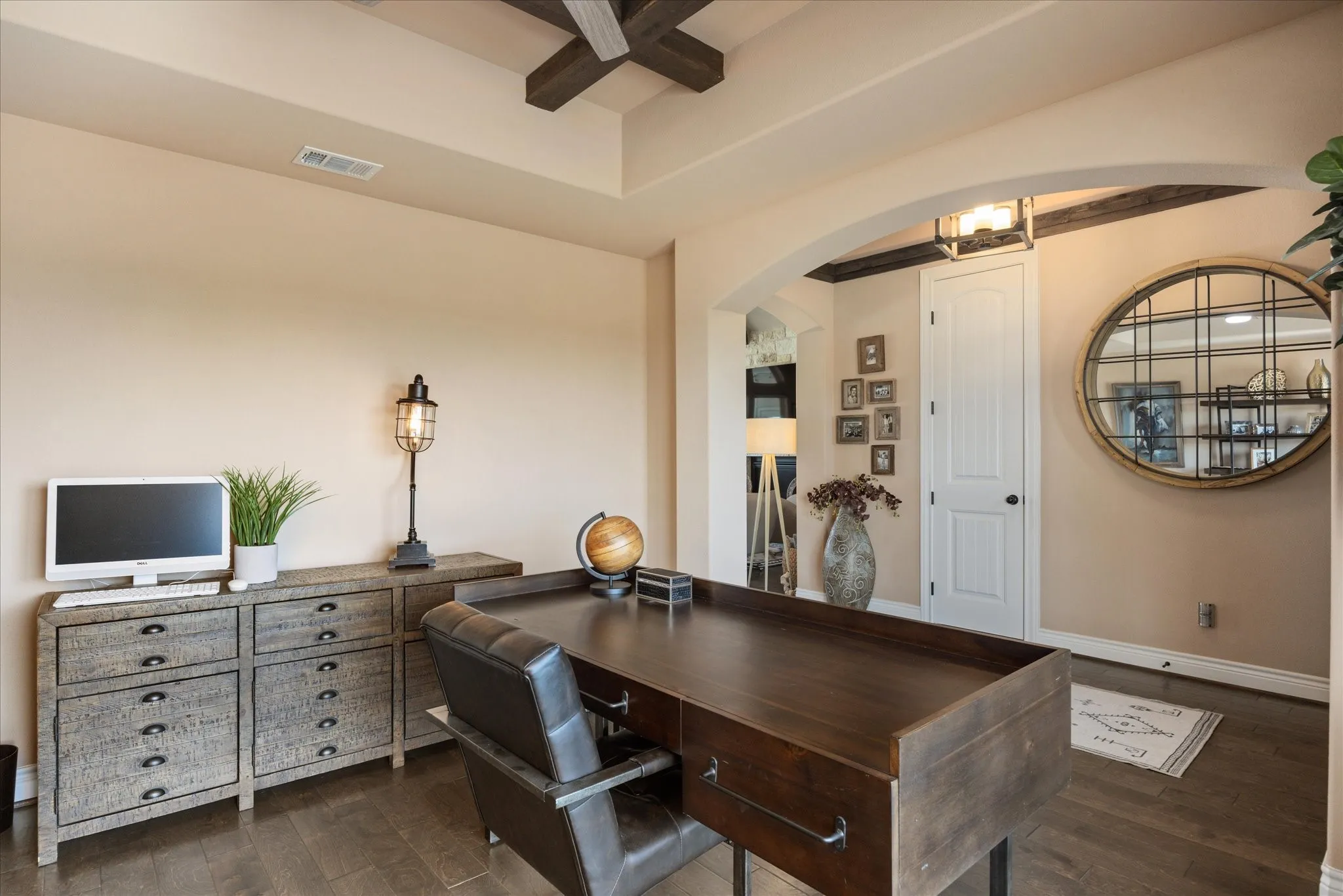 Tray ceiling with wood-finish beams, wood-finish flooring, arched doorway with wood-finish trim, paneled interior door, and integrated lighting fixture