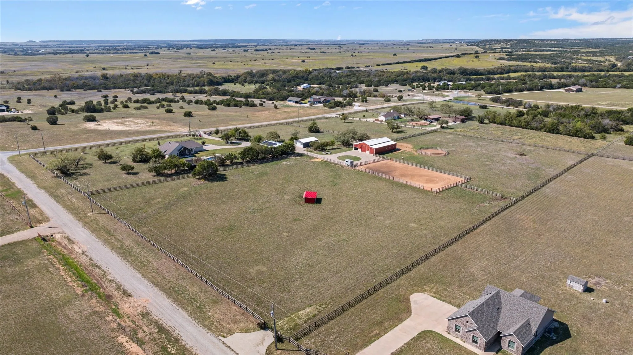 Expansive property featuring an equestrian arena, a red barn, and a gravel road