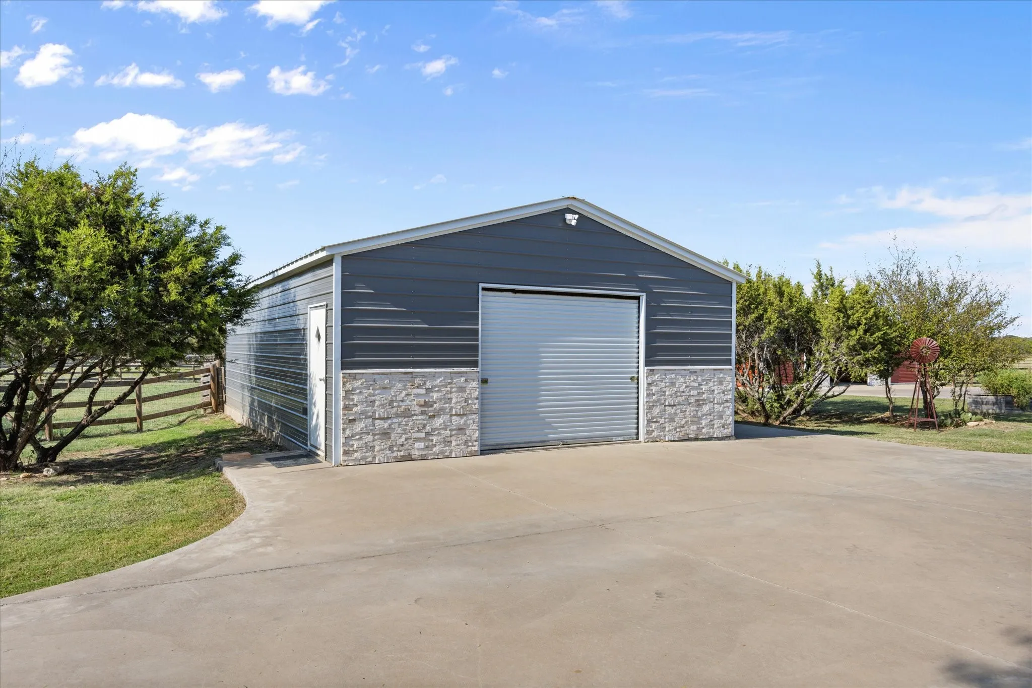 Metal outbuilding with a roll-up garage door, stone veneer accents, and a pedestrian entry door