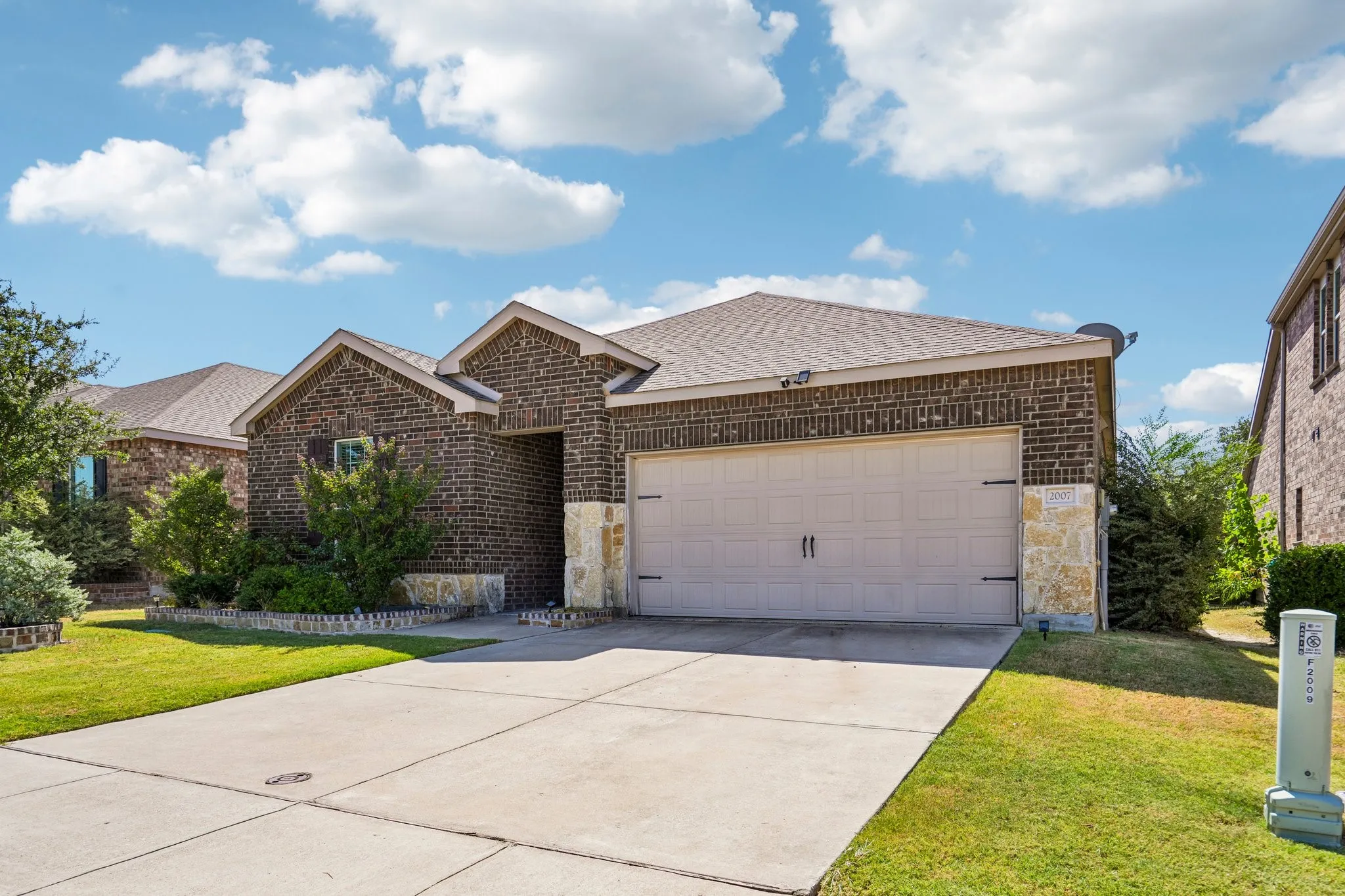 Brick exterior with stone accents, attached garage with carriage-style hardware, concrete driveway, and established landscaping