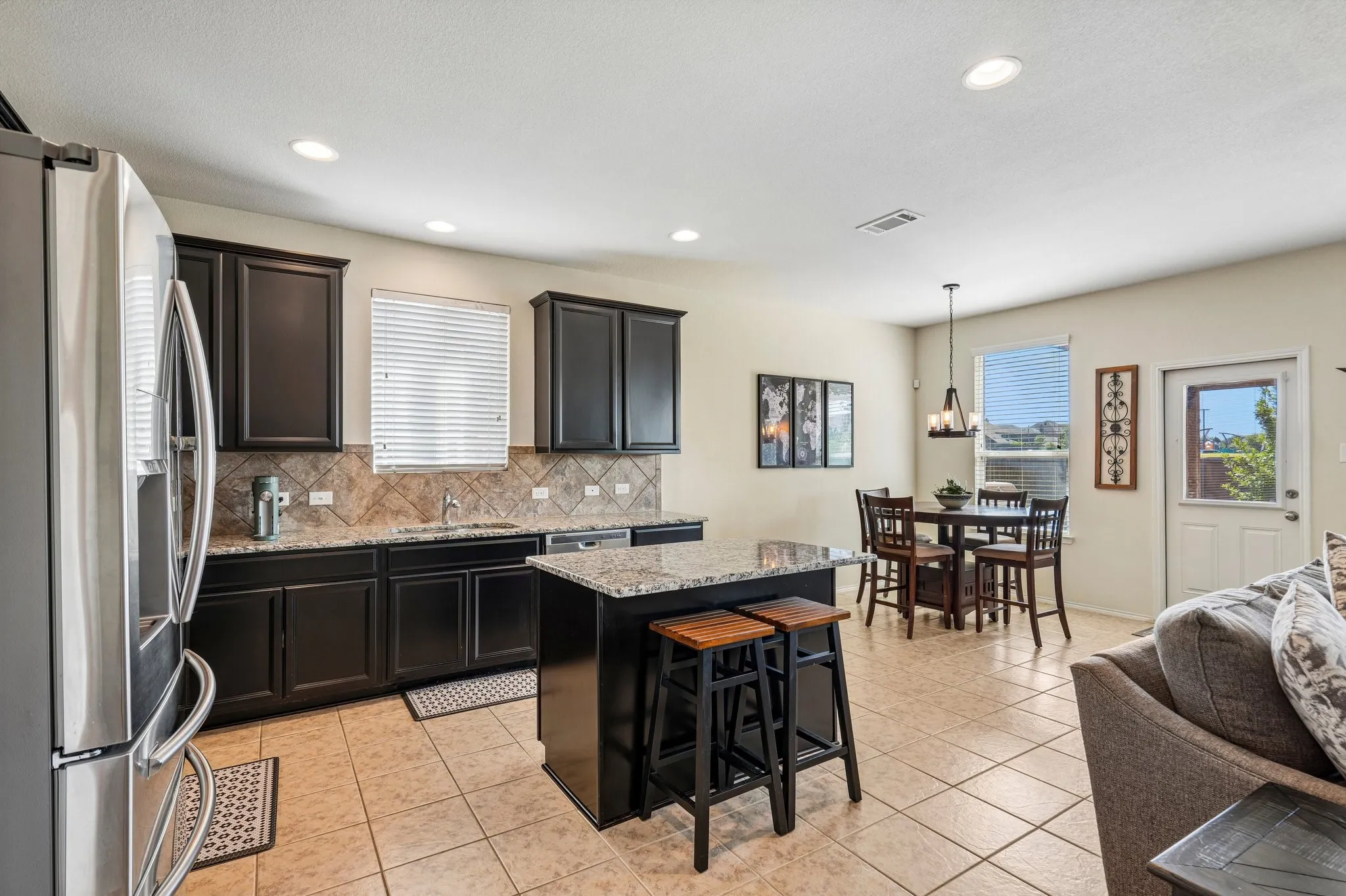Kitchen featuring dark wood cabinetry, a center island with a granite countertop, a stainless steel refrigerator, and tile flooring