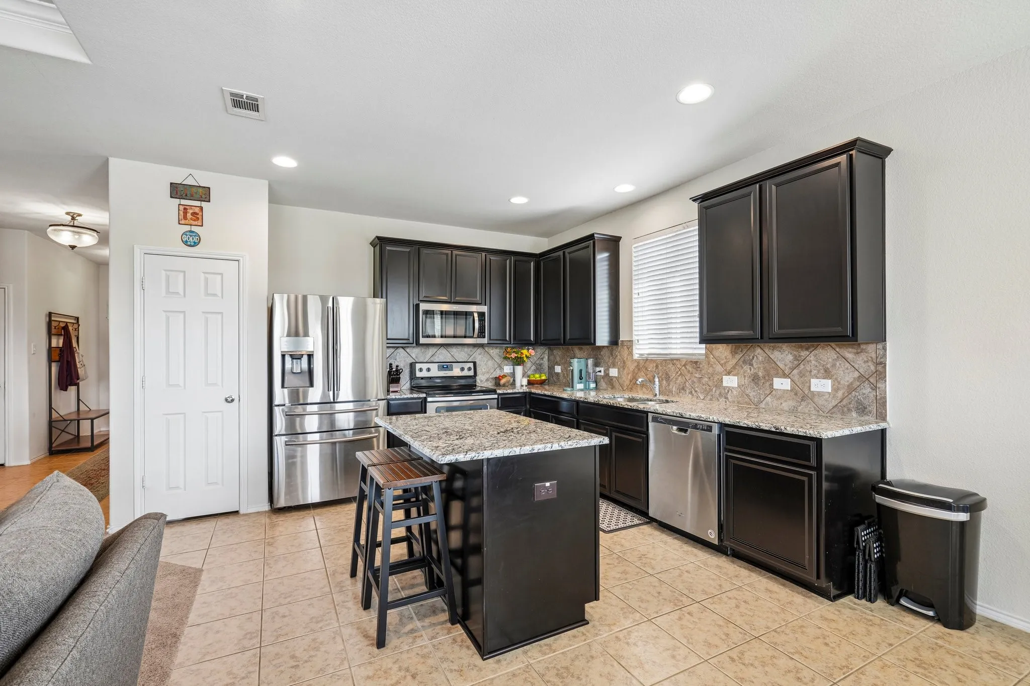 Kitchen featuring dark wood cabinetry, granite countertops, tile backsplash, and stainless-steel appliances