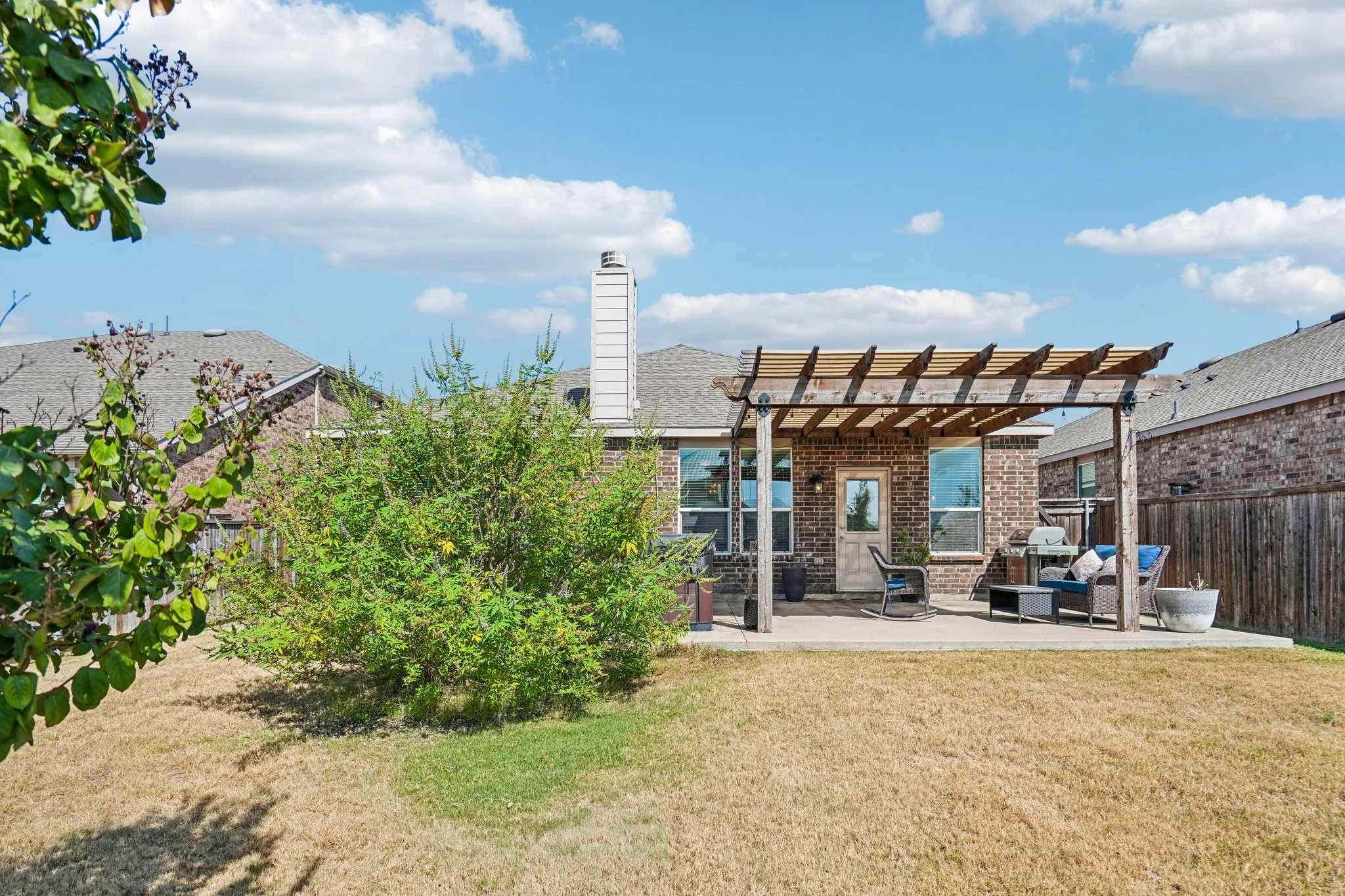 Brick exterior with a pergola-covered patio, surrounded by a wood fence, and featuring a prominent chimney